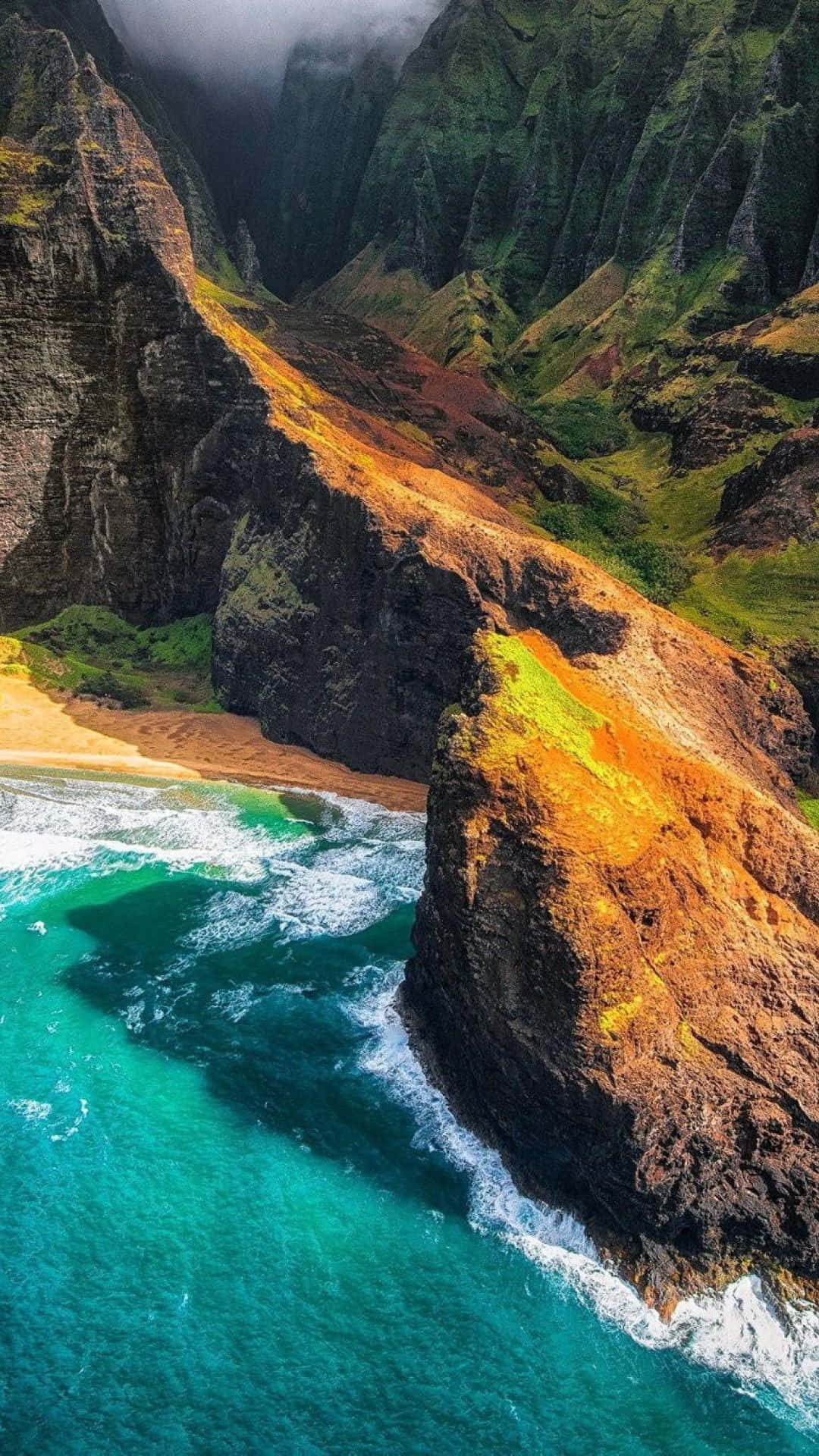 Hawaii iPhone 桌布 壁紙 — 從高空俯瞰，一個隱藏在高聳綠色和橙色懸崖之間的僻靜海灘，下方有藍綠色海浪拍打。