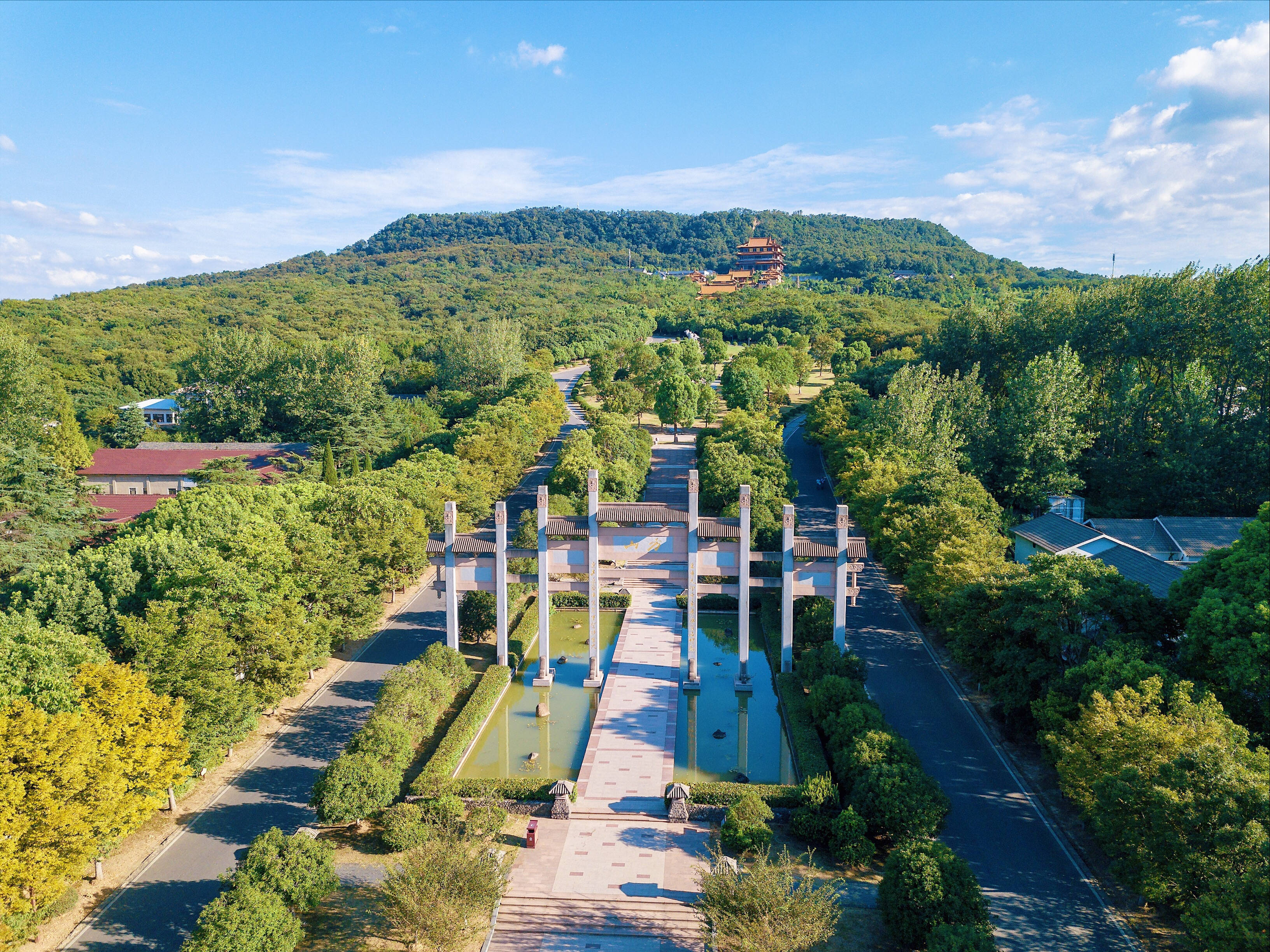 Nanjing 桌布 壁紙 — 從高空俯瞰，一座宏偉的傳統中式大門兩旁是水道，通往一座位於青翠山頂的寶塔，背景是明亮的藍天。