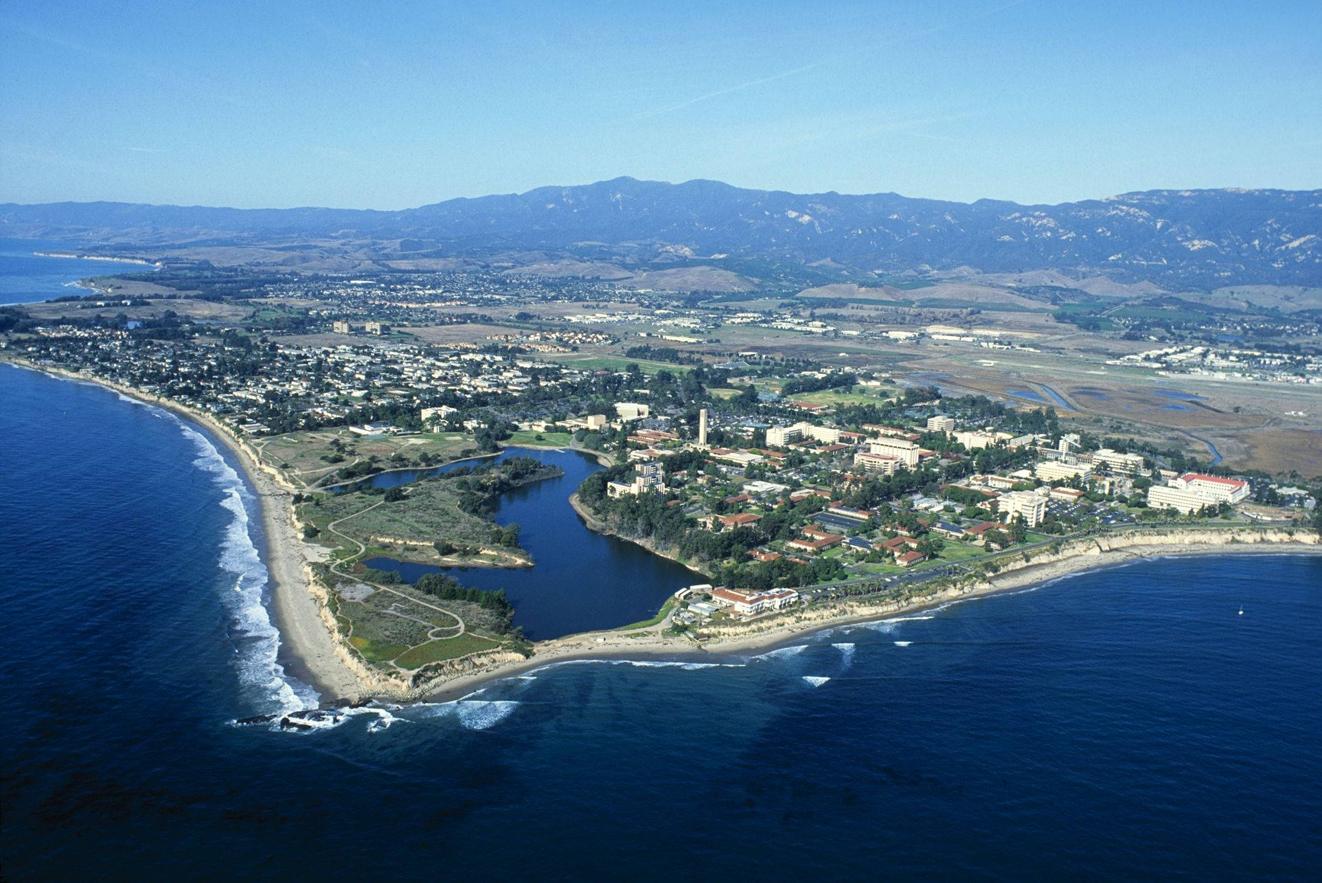 島嶼 桌布 壁紙 — 從高空俯瞰，一座沿海小鎮坐落在深藍色海洋與遠山之間，天空晴朗。