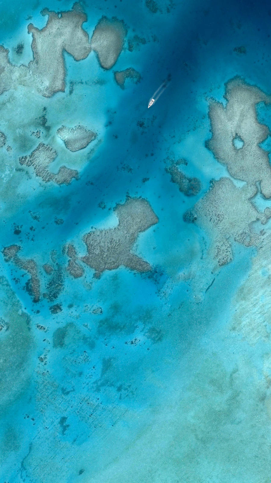 島嶼 桌布 壁紙 — 從高空俯瞰，一艘小船在廣闊珊瑚礁上閃耀的碧綠海水中滑行。