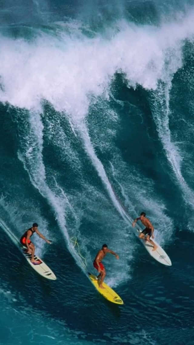 Surfing iPhone 桌布 壁紙 — 從高空俯瞰，三名衝浪者騎乘巨大的藍綠色海浪，周圍白色泡沫四濺。