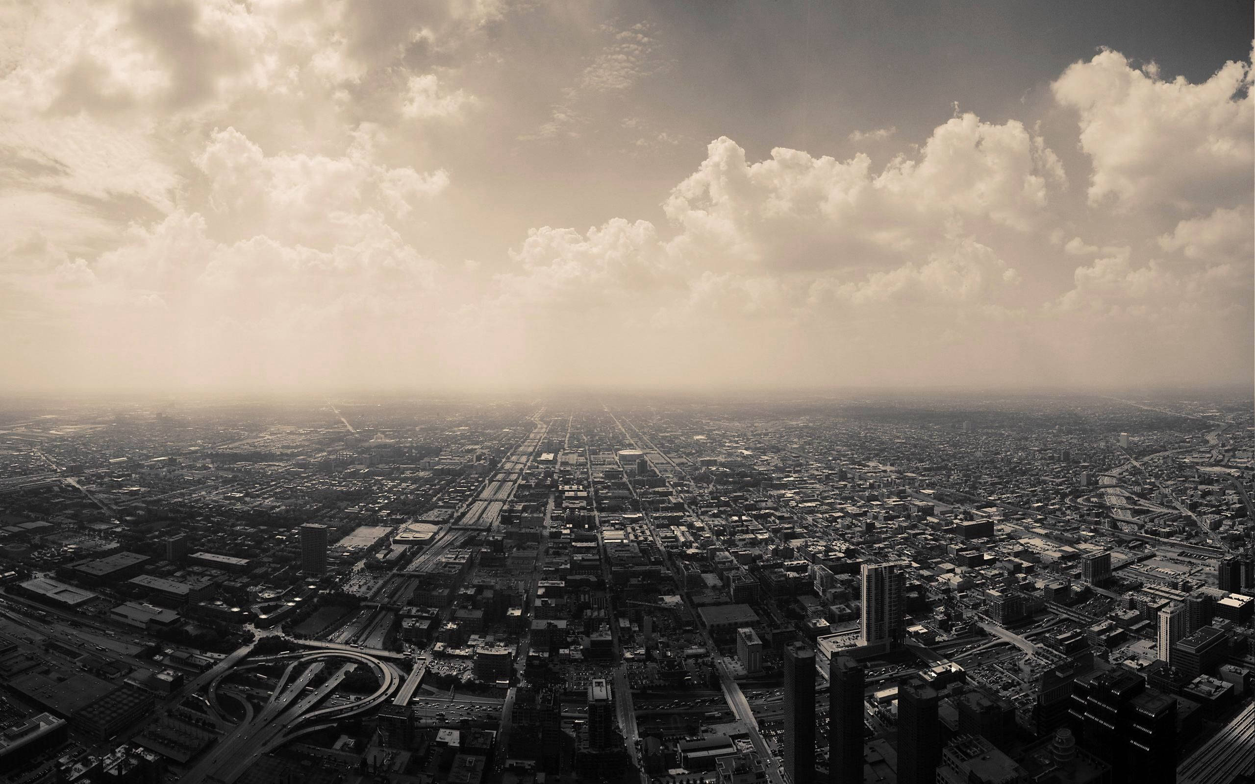 城市風景 桌布 壁紙 — 從高空俯瞰，在戲劇性的多雲天空下，廣闊的城市景觀呈現懷舊的棕褐色調和朦朧的氛圍。
