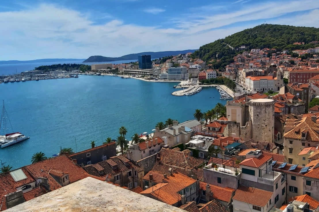 Croatia 桌布 壁紙 — 從高空俯瞰，在明亮的藍天下，一座沿海小鎮的赤陶屋頂緊擁著碧綠的海水。