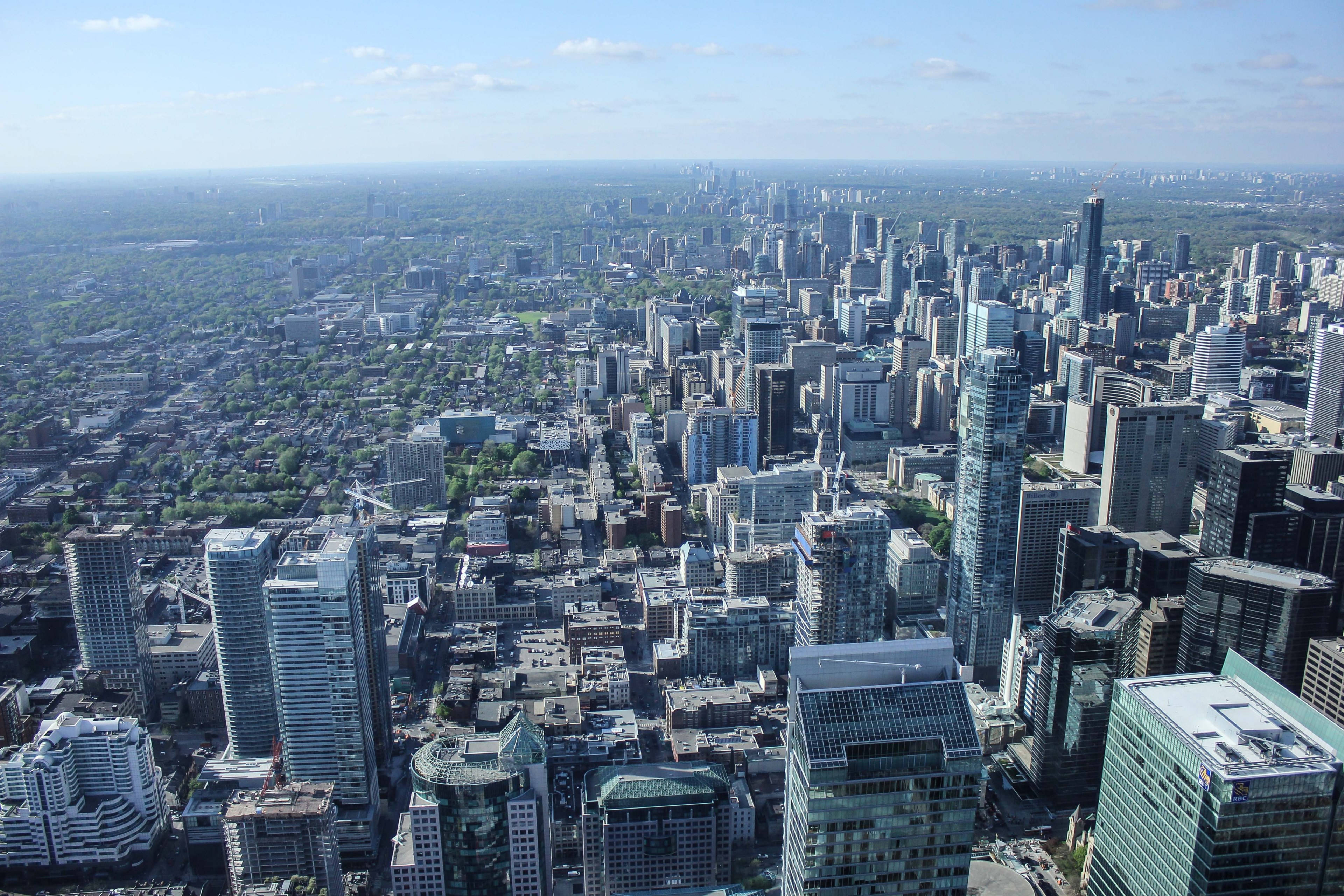 View 桌布 壁紙 — 從高空俯瞰，在明亮的藍天下，一座現代化城市景觀延伸開去，玻璃摩天大樓與綠色公園交織。