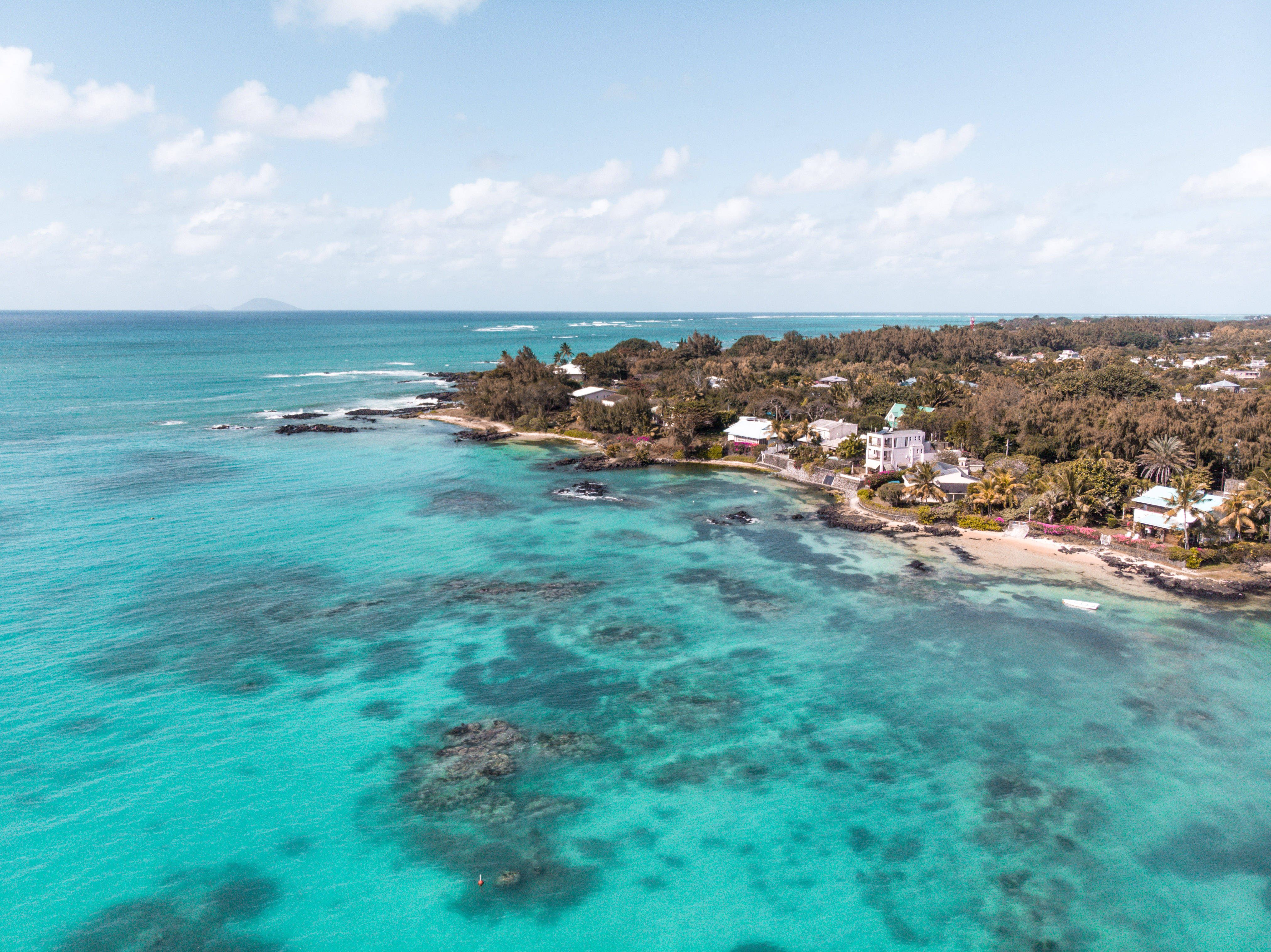 Mauritius 桌布 壁紙 — 從高空俯瞰，在明亮的藍天下，綠松石色的加勒比海水拍打著鬱鬱蔥蔥的海岸線，點綴著熱帶房屋和棕櫚樹。