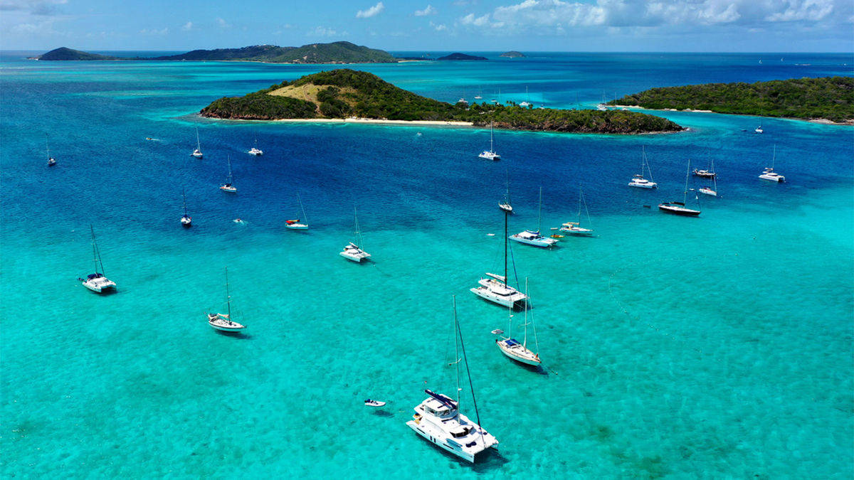 St Vincent And The Grenadines 桌布 壁紙 — 從高空俯瞰，在明亮的藍天下，翠綠島嶼周圍點綴著帆船的碧綠海水。