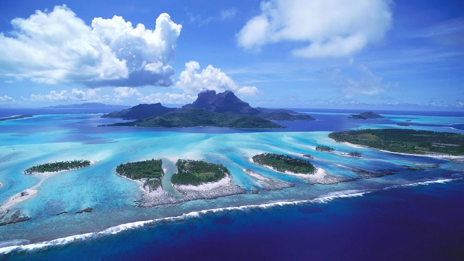 Islands 桌布 壁紙 — 從高空俯瞰，在明亮的藍天和蓬鬆的白雲下，碧綠色的潟湖和鬱鬱蔥蔥的綠色島嶼。