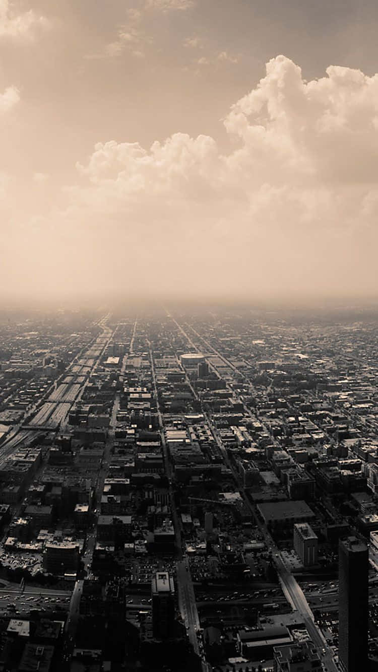 City iPhone 桌布 壁紙 — 從高空俯瞰，在朦朧的棕褐色天空和戲劇性的雲層下，廣闊的城市景觀。