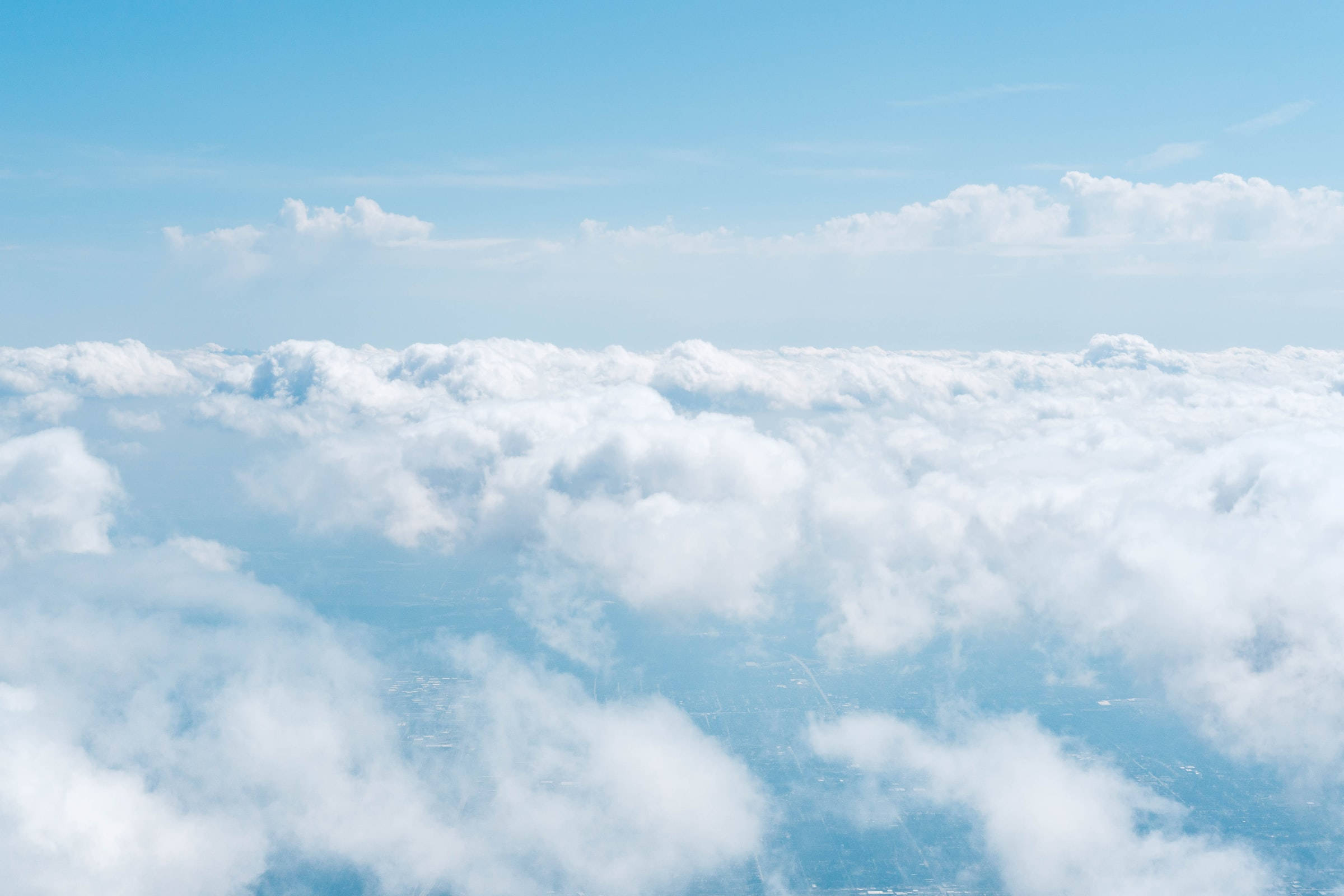 雲朵 桌布 壁紙 — 從高空俯瞰，在清澈藍天下翱翔於無盡蓬鬆白雲之上，遠方陸地清晰可見。