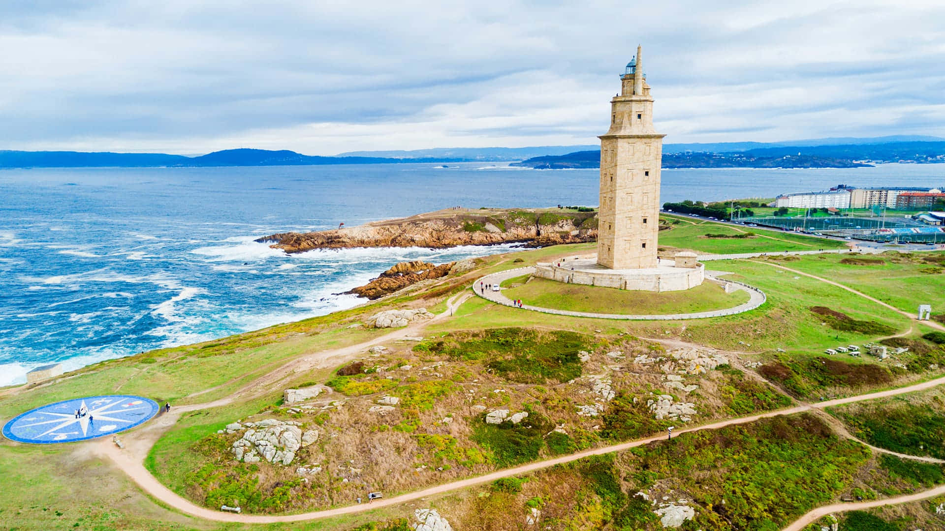 Lighthouse 桌布 壁紙 — 從高空俯瞰，埃庫萊斯燈塔矗立在長滿青草的海岸懸崖上，俯瞰著藍色海洋，下方波濤洶湧。