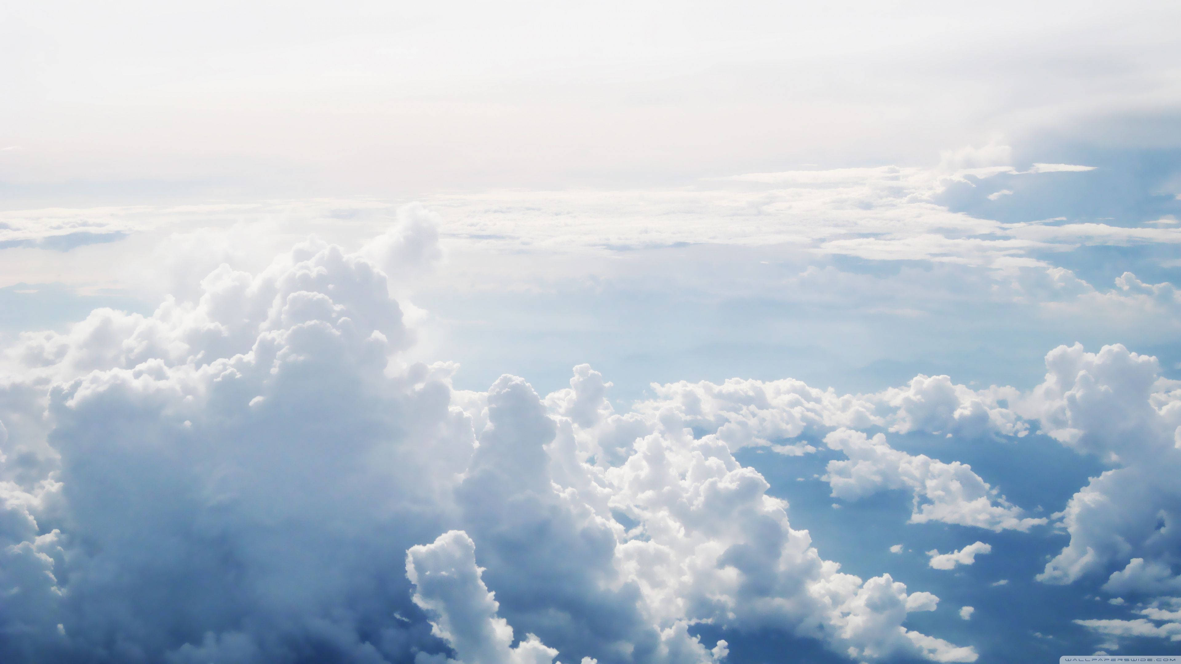 Aesthetic Cloud 桌布 壁紙 — 從高空俯瞰，大片蓬鬆的白雲在深藍色的天空中飄動，柔和的陽光穿透雲層。