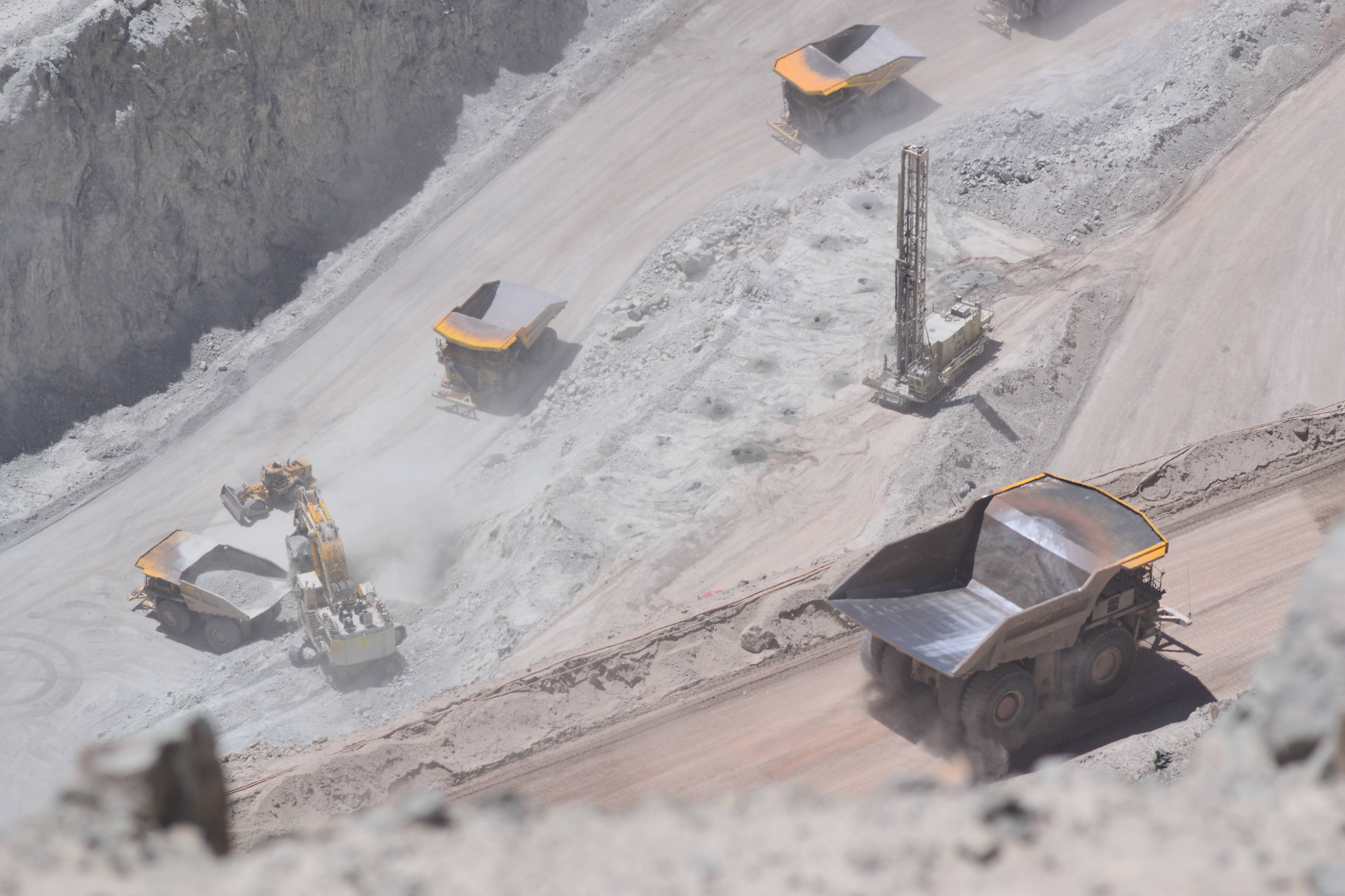 Mining 桌布 壁紙 — 從高空俯瞰，巨大的自卸卡車和挖掘機在塵土飛揚的露天礦場中，於明亮的日光下移動泥土。