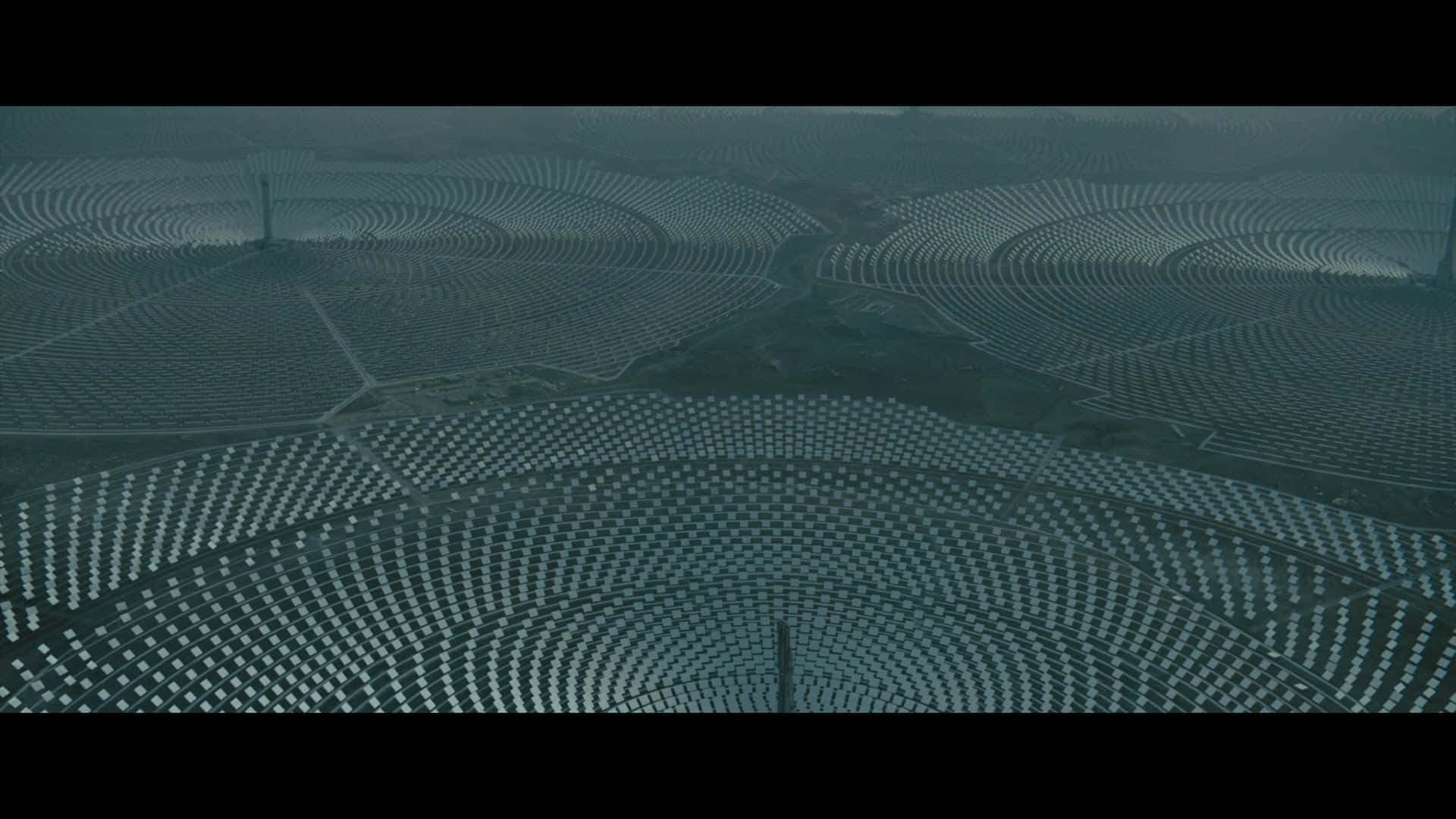 銀翼殺手2049 桌布 壁紙 — 從高空俯瞰，廣闊的彎曲太陽能農場在陰天籠罩下，延伸至霧氣瀰漫的景觀。