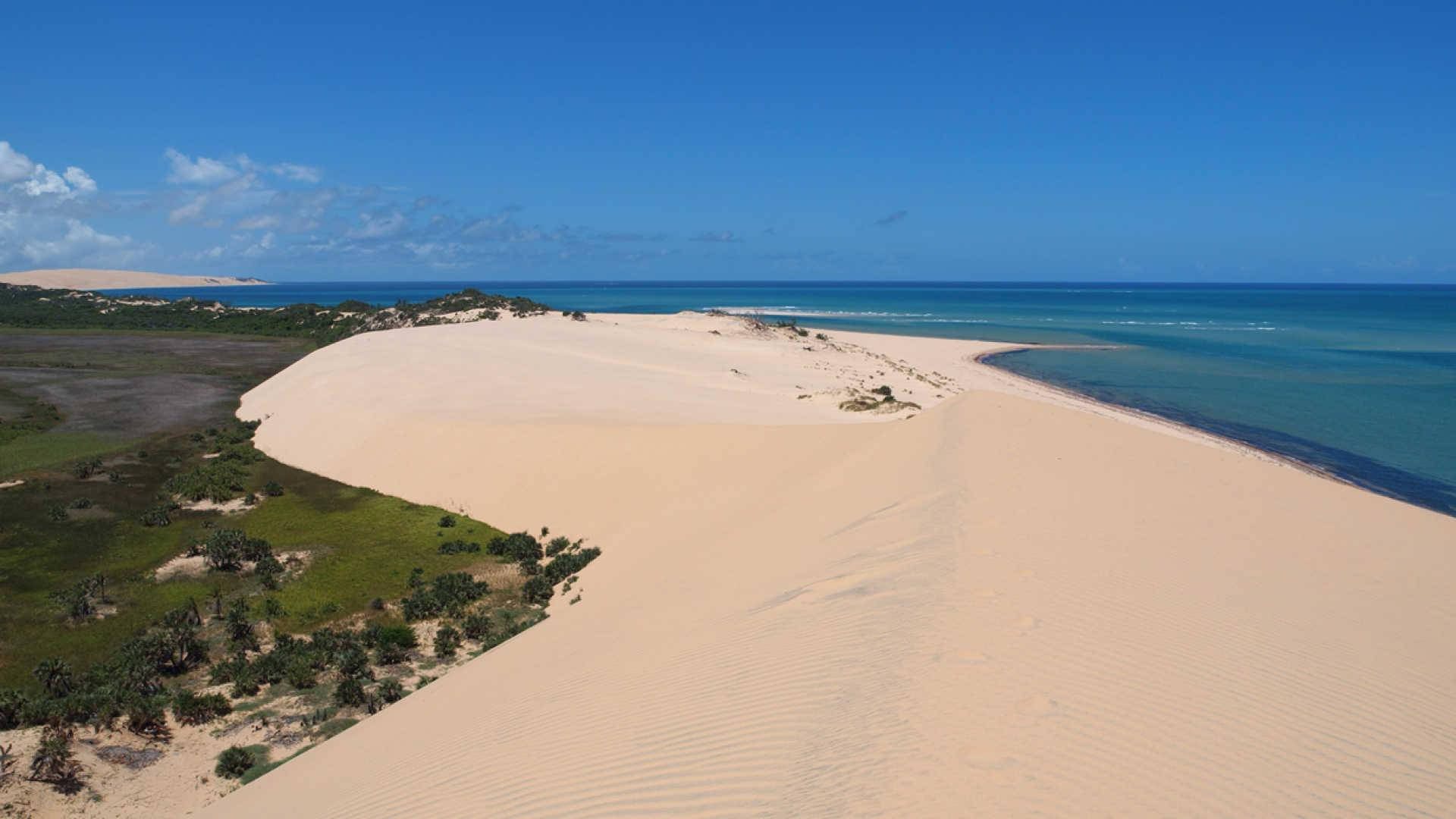 Mozambique 桌布 壁紙 — 從高空俯瞰，廣闊的金色沙丘在晴朗藍天和零星白雲下蜿蜒向藍綠色海洋延伸。