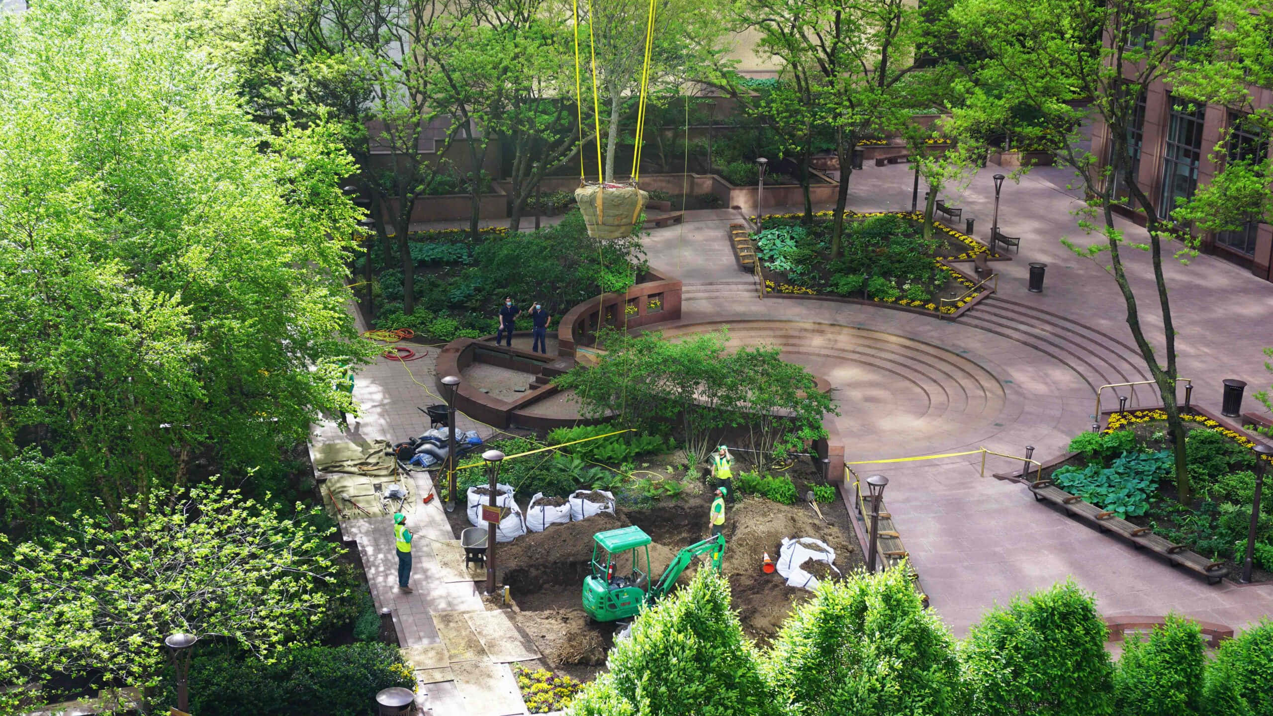 風景 桌布 壁紙 — 從高空俯瞰，建築工人正在一個綠意盎然的城市公園中安裝一塊大石頭，公園內有彎曲的小徑和梯田花園。