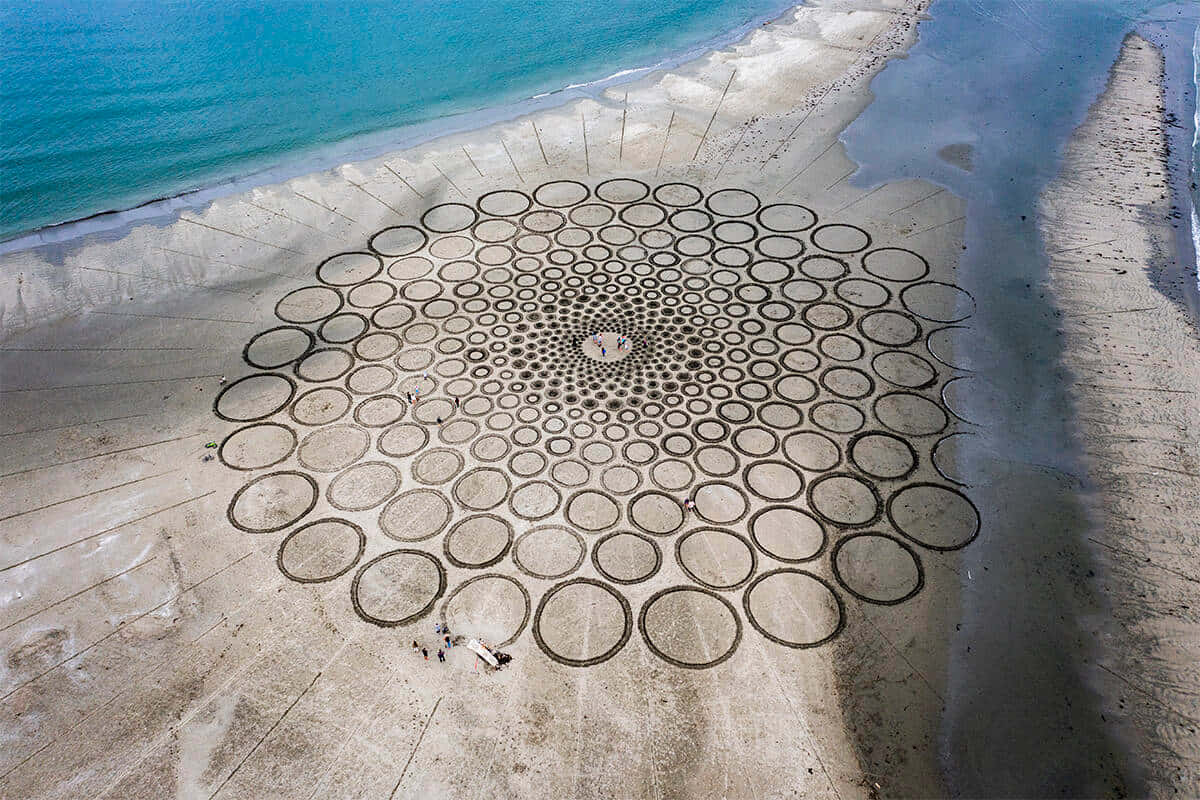 Sand Art 桌布 壁紙 — 從高空俯瞰，沙灘上刻有巨大的幾何圓形圖案，旁邊是碧綠的海水。