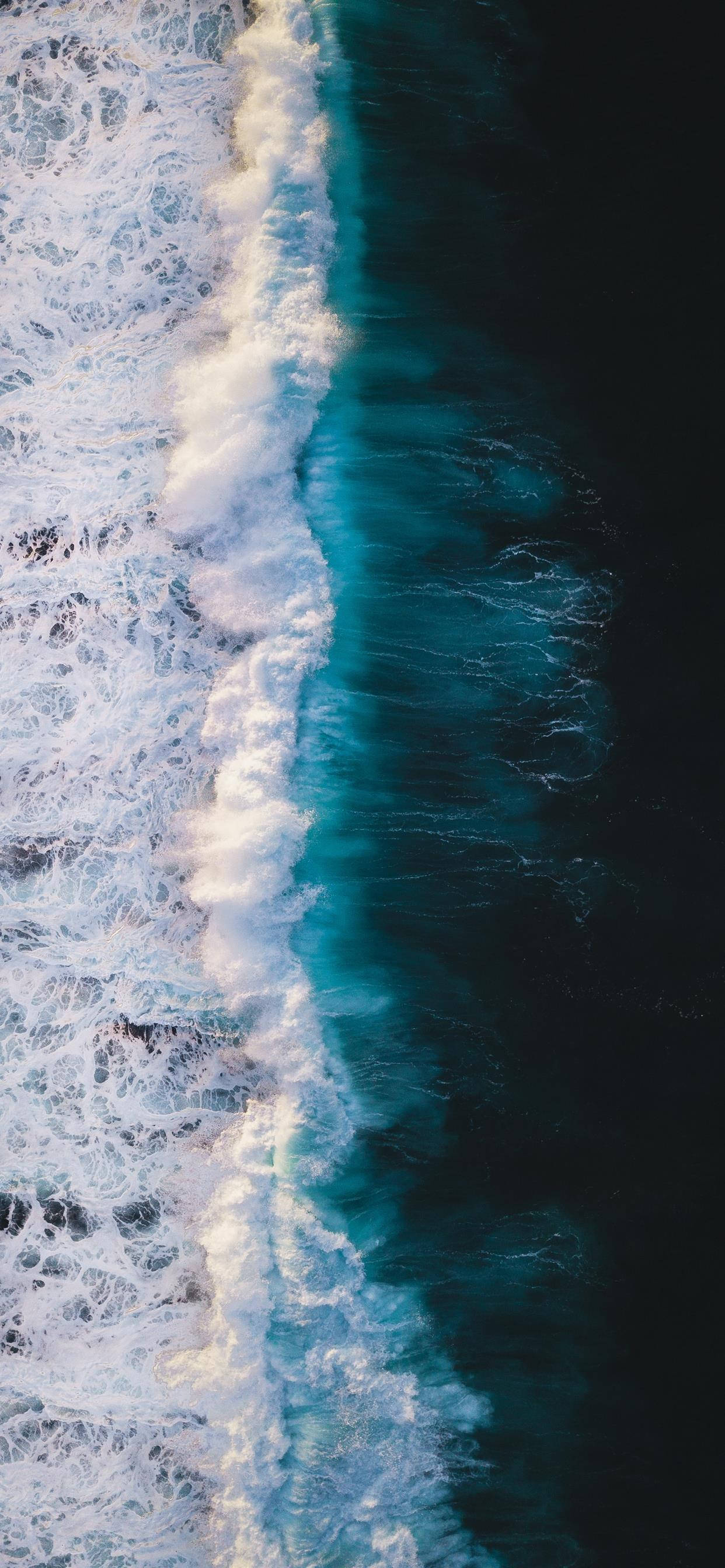 waves 桌布 壁紙 — 從高空俯瞰，海浪撞擊形成一條泡沫般的白線，與深藍綠色和黑色的海水形成對比。