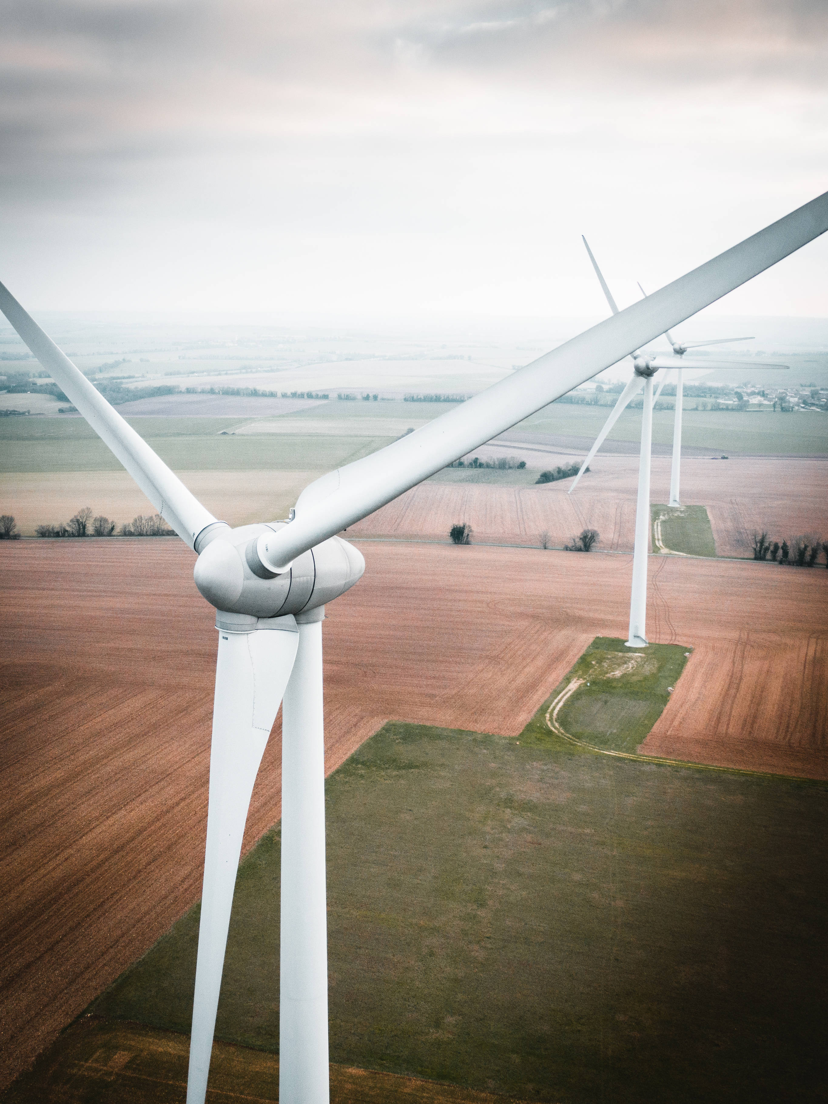 Energy 桌布 壁紙 — 從高空俯瞰，白色風力渦輪機在陰天下的拼布田野中高高聳立。
