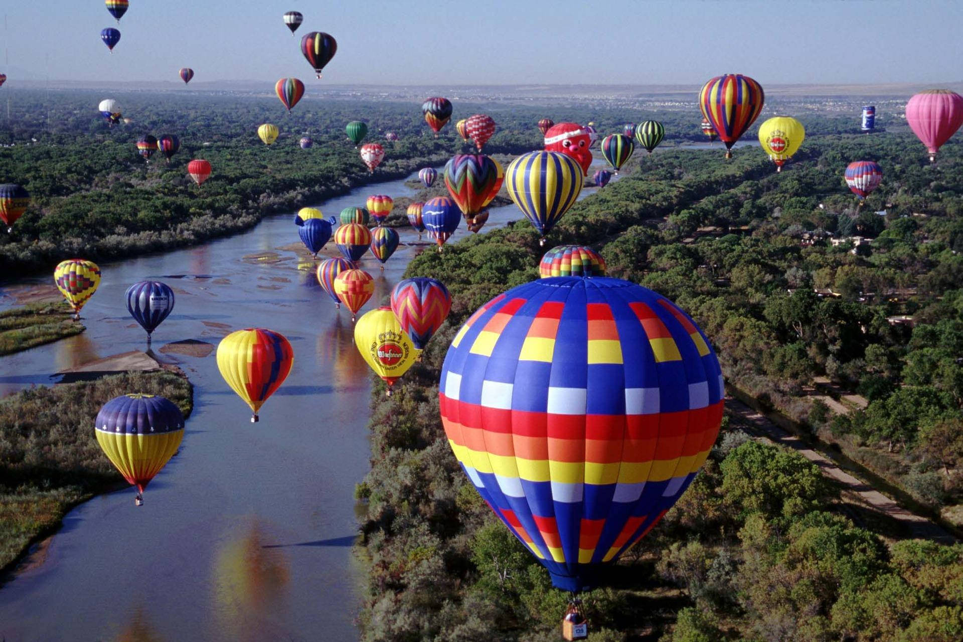 Balloon 桌布 壁紙 — 從高空俯瞰，眾多色彩繽紛的熱氣球漂浮在蜿蜒的河流上方，周圍是茂密的綠色森林。