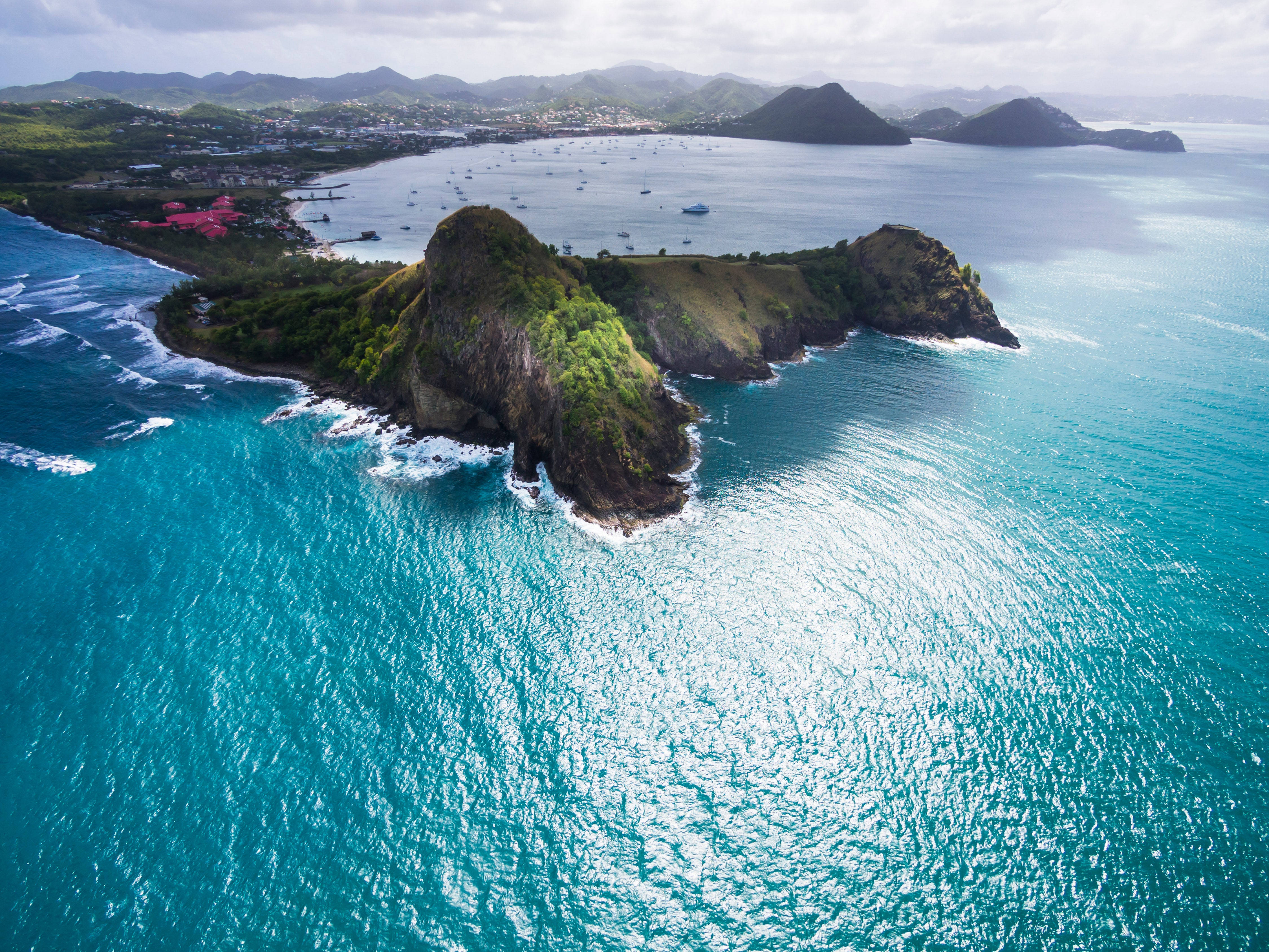 島嶼 桌布 壁紙 — 從高空俯瞰，碧綠的海水拍打著鬱鬱蔥蔥的懸崖，遠處島嶼和沿海城鎮在陰天之下。