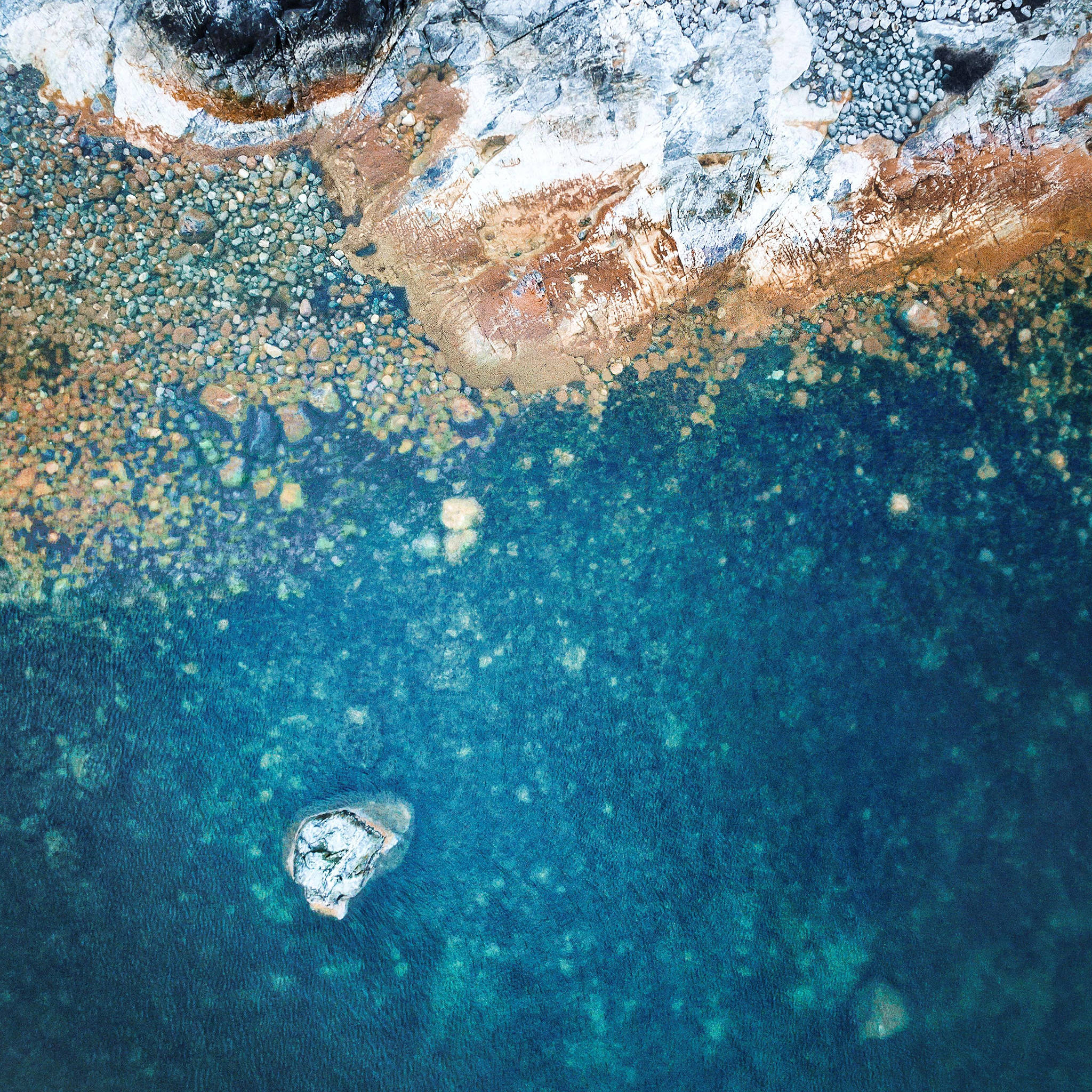 美學 iPad 壁紙 桌布 壁紙 — 從高空俯瞰，碧綠的海水與崎嶇的岩石海岸線交匯，散落著鵝卵石和一個小島。