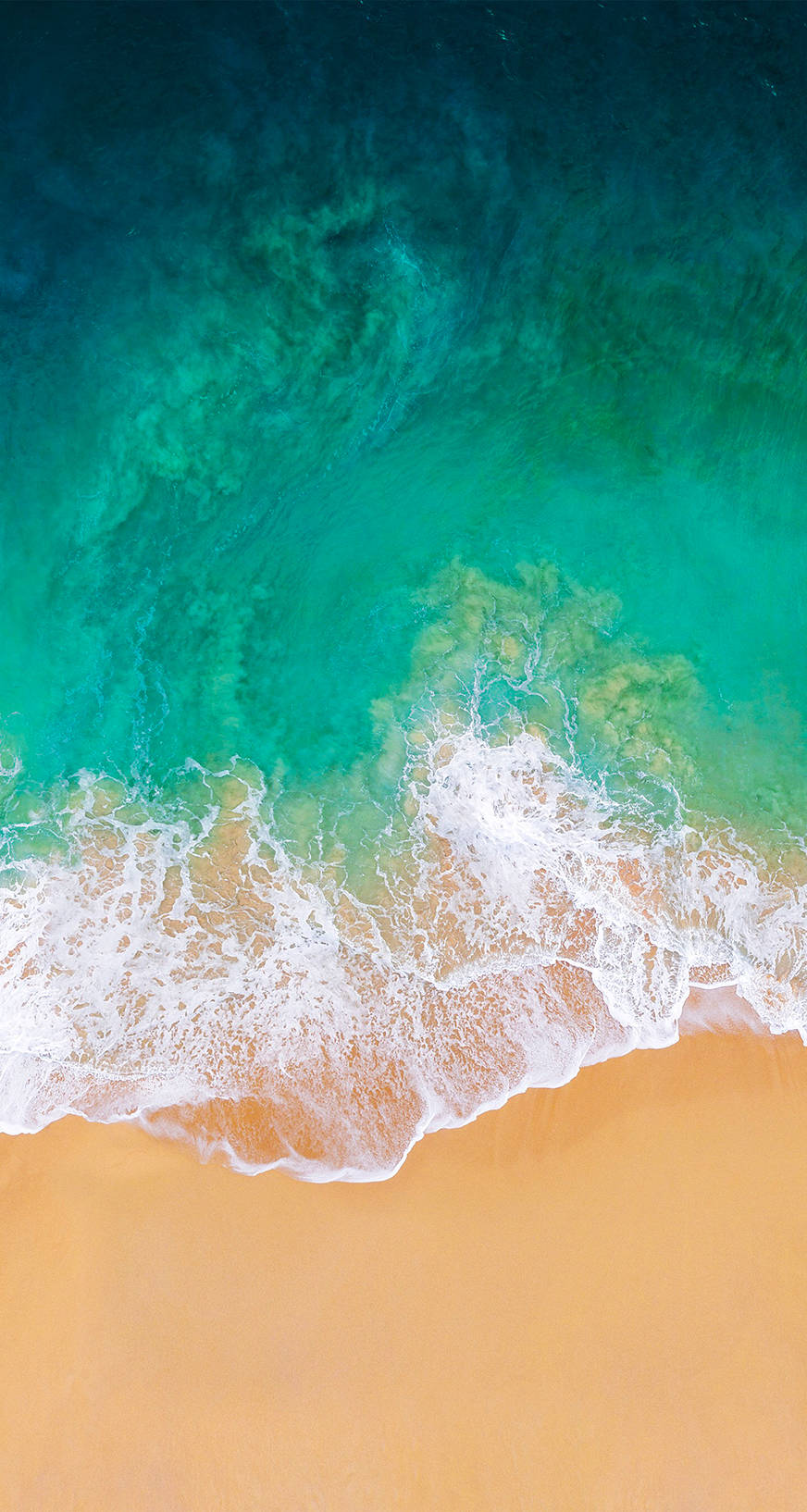 iOS 11 桌布 壁紙 — 從高空俯瞰，碧綠的海浪拍打著金色沙灘，呈現出鮮豔的漸變色調。