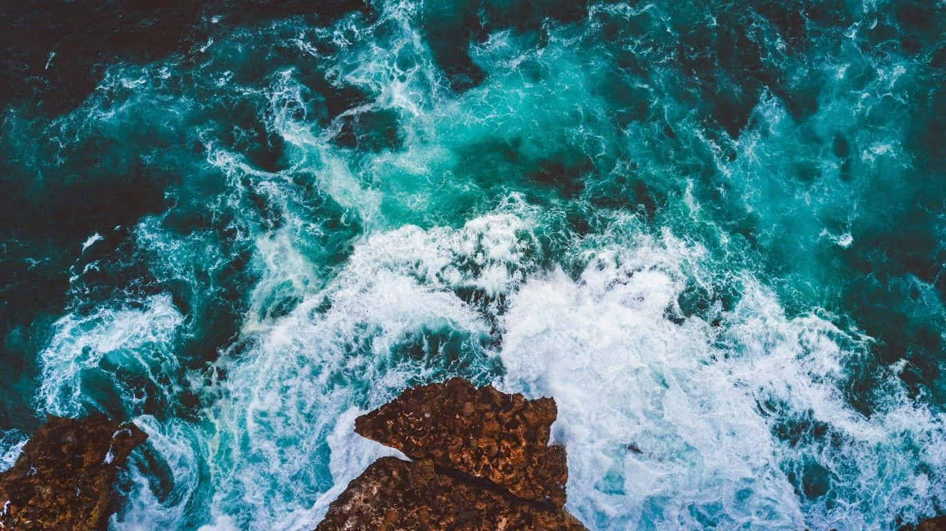 Sea 桌布 壁紙 — 從高空俯瞰，碧綠色的海浪拍打著崎嶇的棕色岩石，激起白色泡沫。