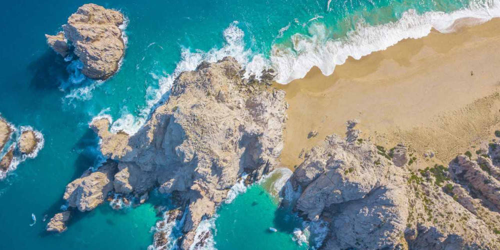 島嶼 桌布 壁紙 — 從高空俯瞰，碧綠色的海浪拍打著崎嶇的懸崖，旁邊是金色的沙灘。