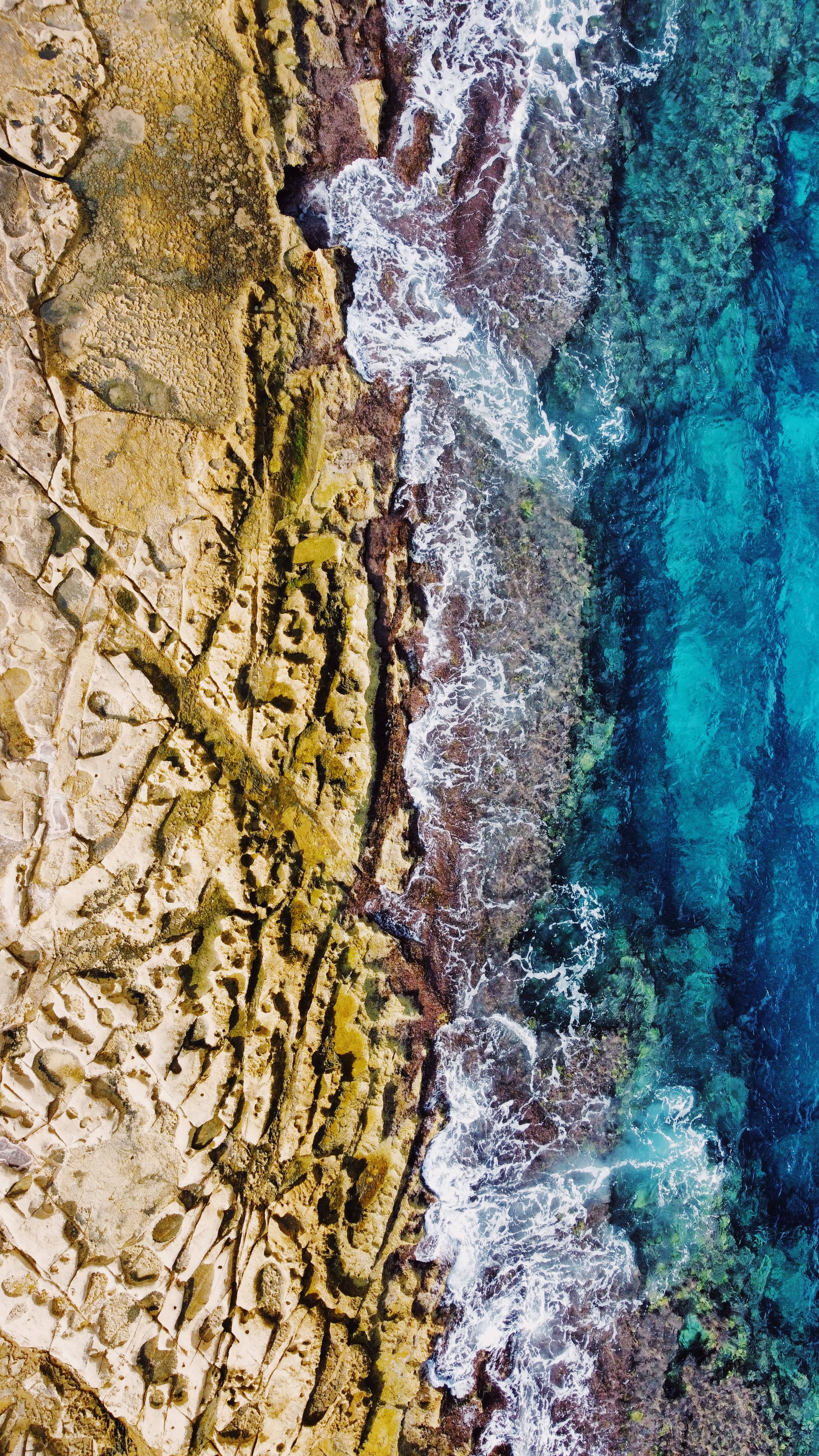 Malta 桌布 壁紙 — 從高空俯瞰，碧綠色的海浪拍打著崎嶇的金棕色懸崖，懸崖上有紋理豐富的岩石結構。