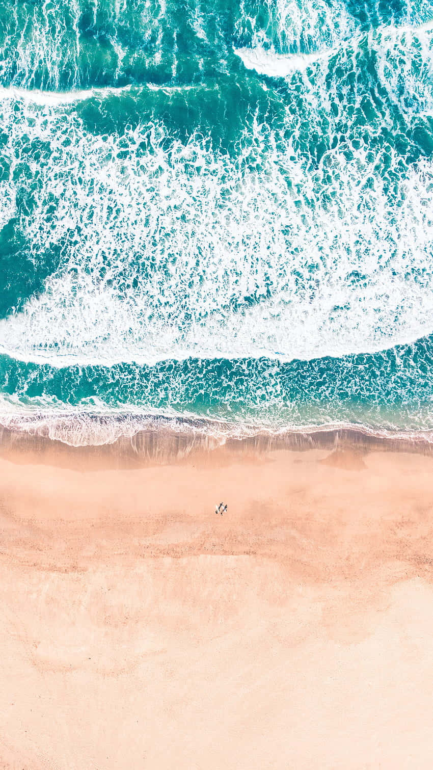Cute Beach iPhone 桌布 壁紙 — 從高空俯瞰，碧綠色的海浪拍打著柔軟的蜜桃色沙灘，兩個微小的人影正在海岸線附近漫步。
