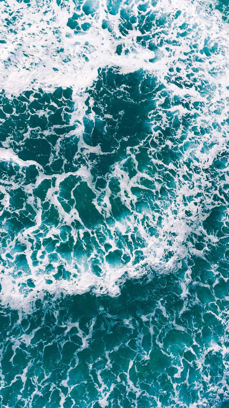 Turquoise iPhone 桌布 壁紙 — 從高空俯瞰，碧綠色的海浪拍打著白色泡沫，形成複雜的圖案。