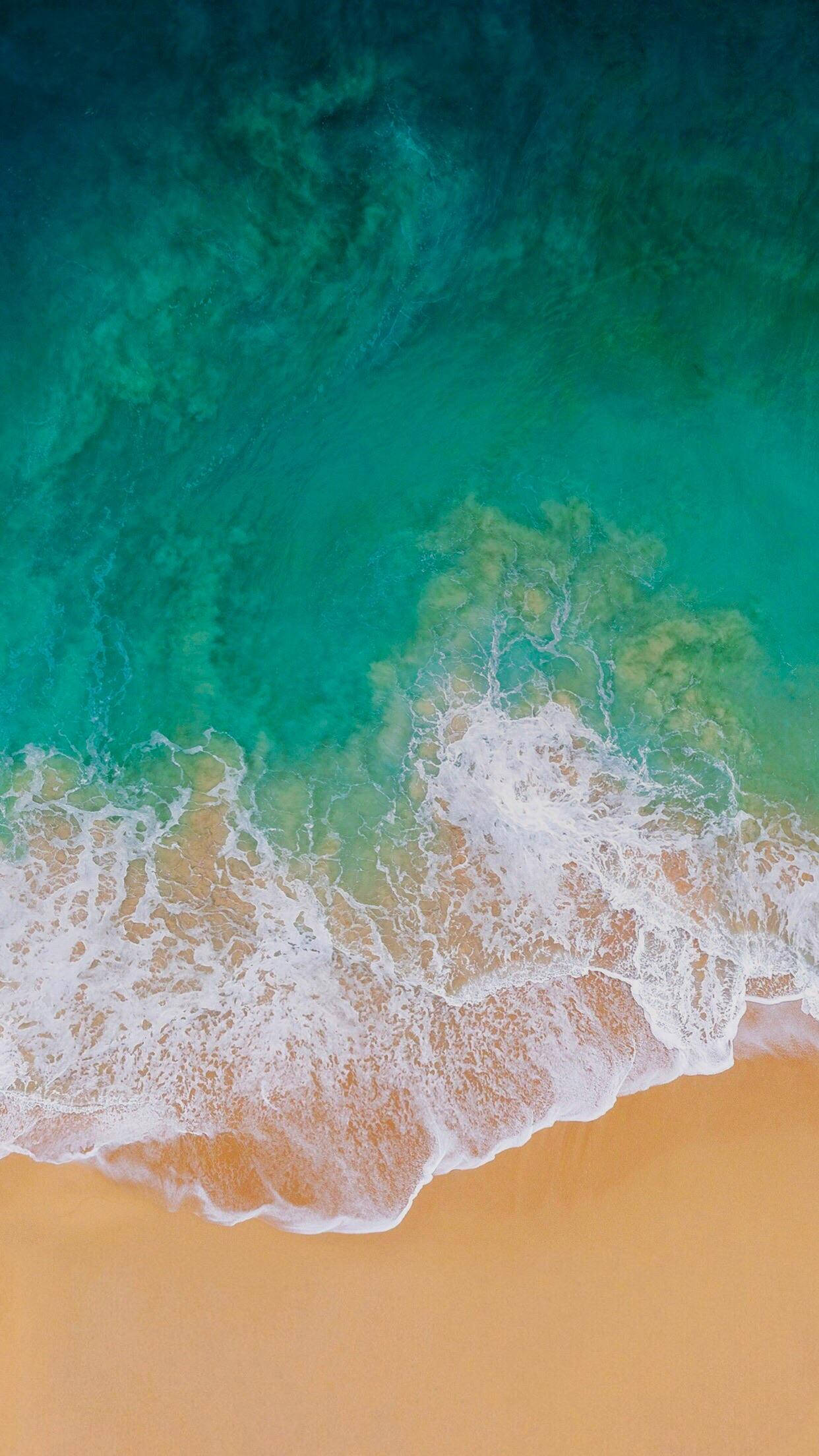 iOS 7 桌布 壁紙 — 從高空俯瞰，碧綠色的海浪拍打著金色沙灘，構成充滿活力的熱帶海灘場景。