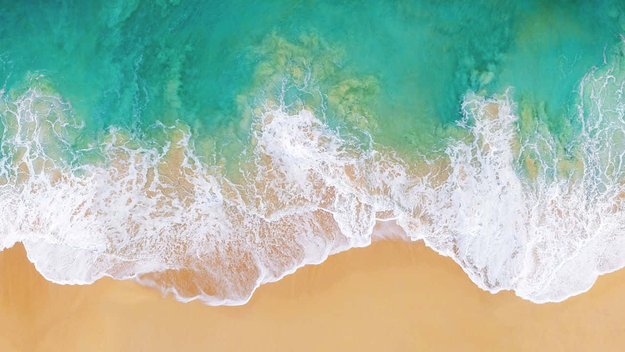 桌布 壁紙 — 從高空俯瞰，碧綠色的海浪拍打著金色沙灘，泛起白色泡沫。