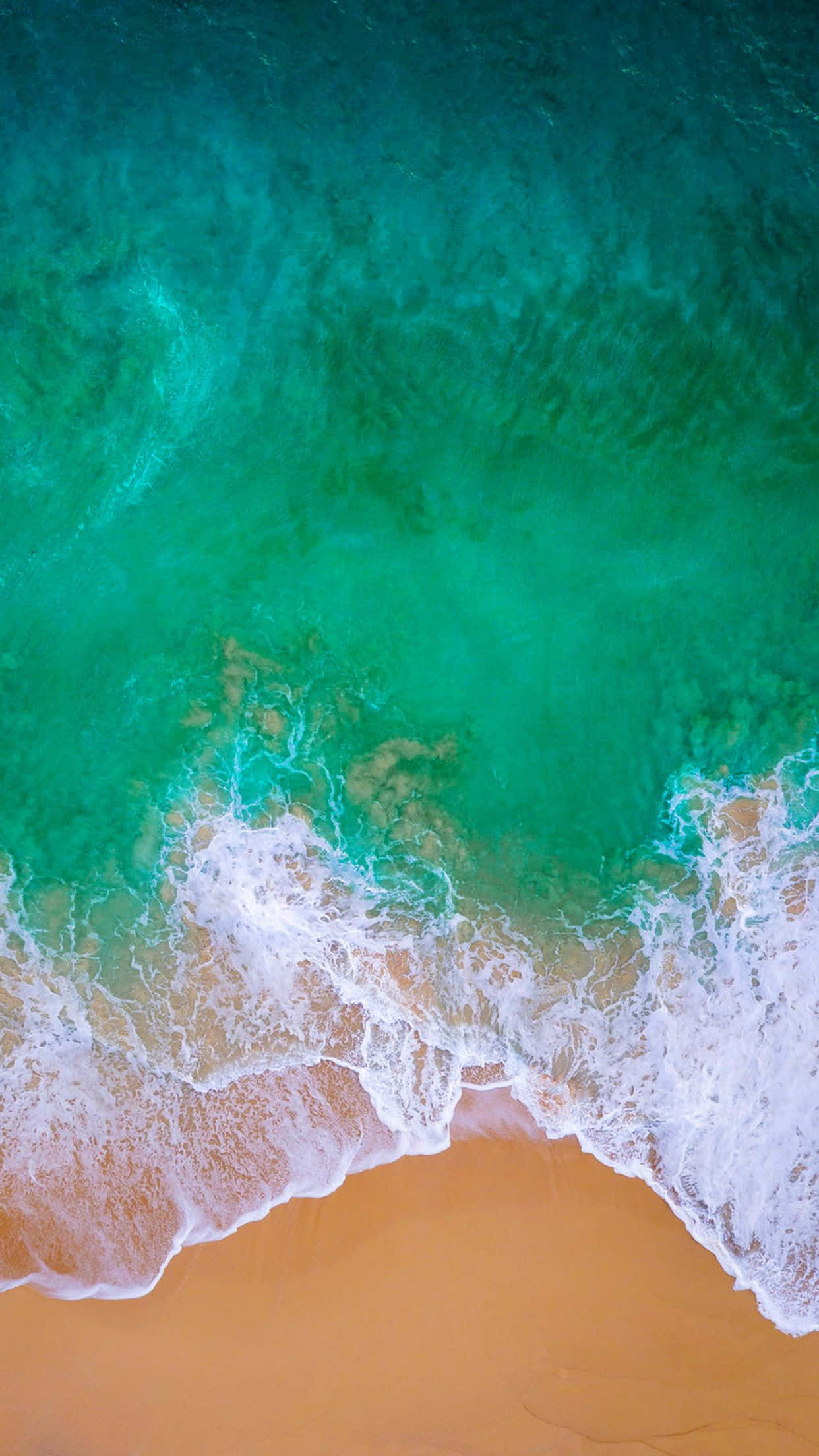 iOS 桌布 壁紙 — 從高空俯瞰，碧綠色的海浪拍打著金色沙灘，泛起白色泡沫的浪花。