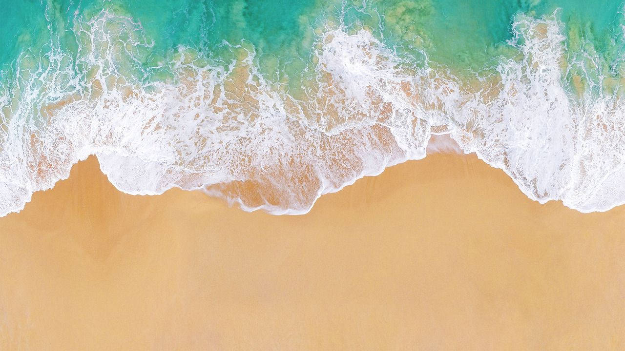 Apple Beach 桌布 壁紙 — 從高空俯瞰，碧綠色的海浪拍打著金色沙灘，呈現寧靜的海岸景色。