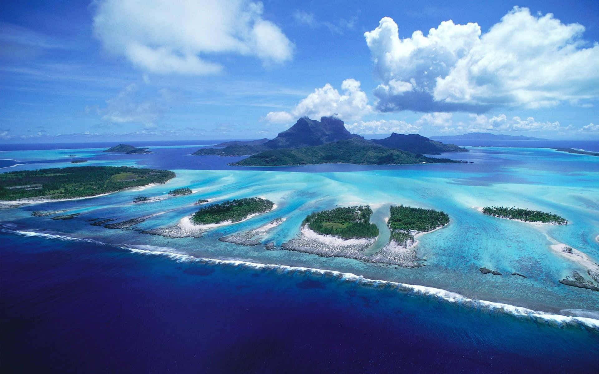 島嶼 桌布 壁紙 — 從高空俯瞰，碧綠色的潟湖和鬱鬱蔥蔥的綠色島嶼被深藍色的海洋環繞，天空明亮，雲朵蓬鬆。