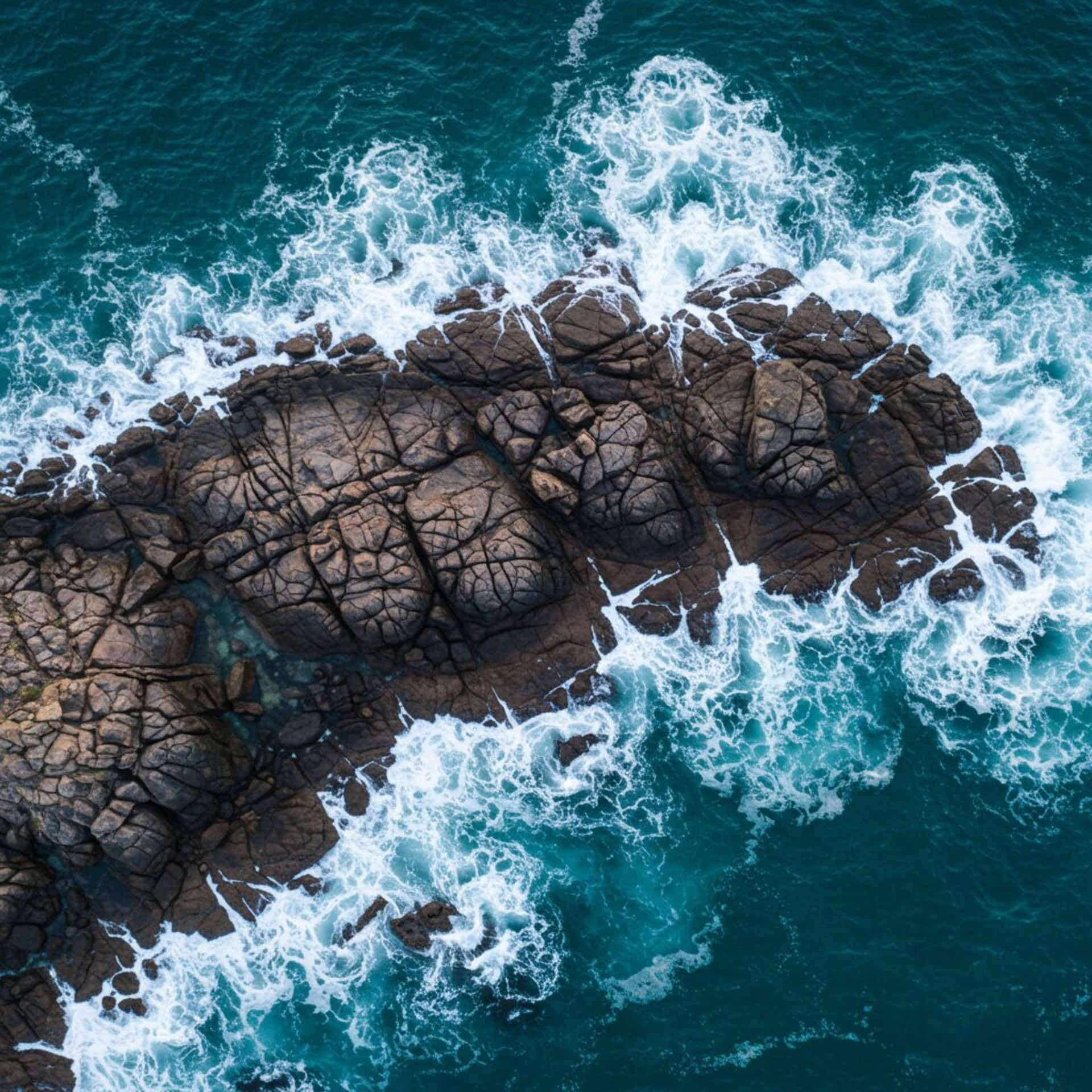 Sea and rocks from above 壁紙 — 從高空俯瞰，綠松石色的海浪拍打著崎嶇的深棕色岩石，形成鋸齒狀的海岸線。