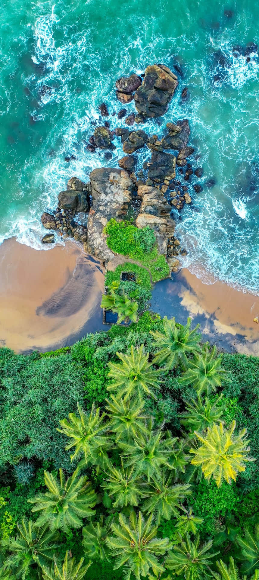 熱帶海灘的空中俯瞰，棕櫚樹和碧綠的海浪拍打岩石。 — 烏賈因 馬哈卡爾 壁紙