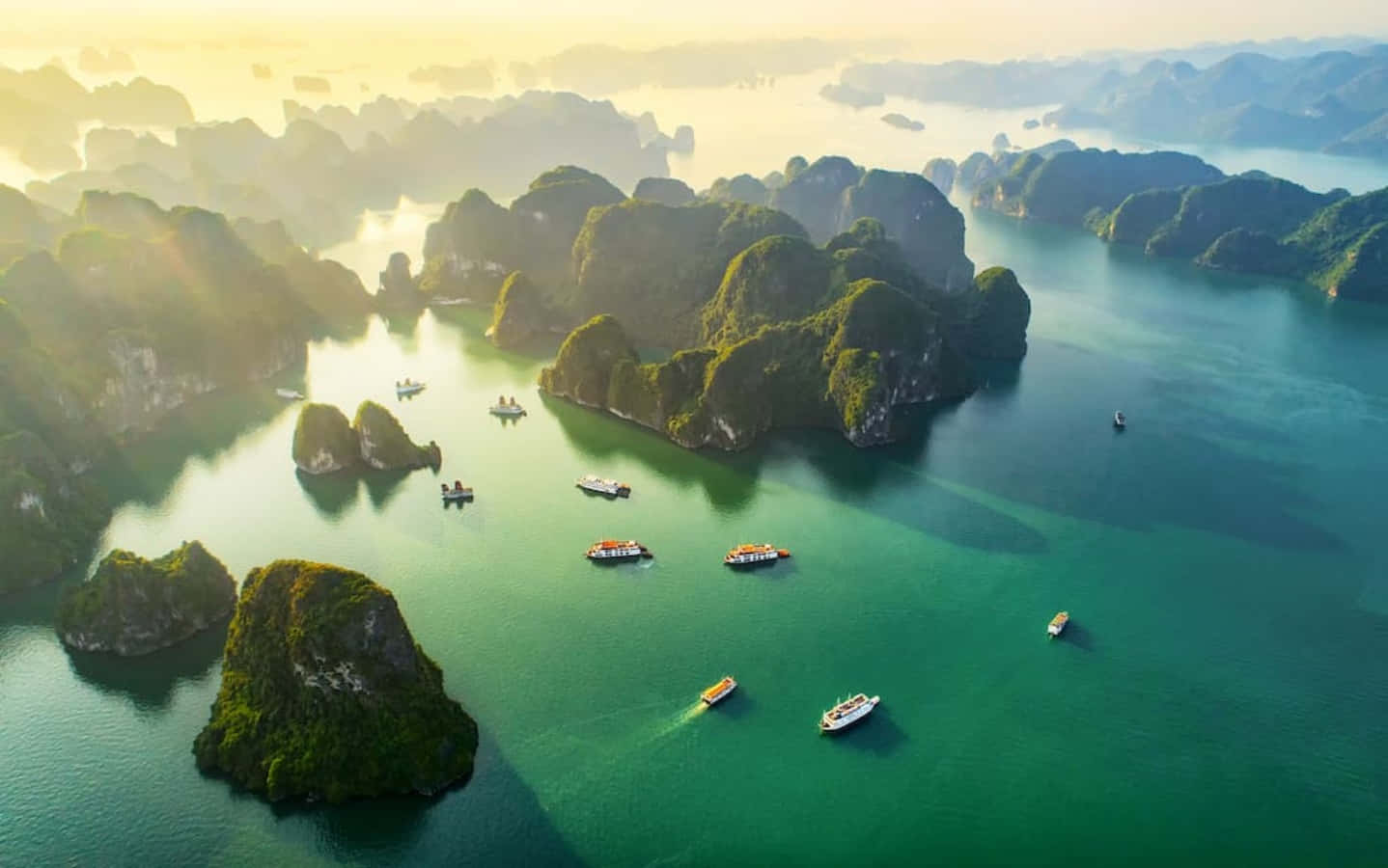 越南 桌布 壁紙 — 從高空俯瞰，翠綠色的海水點綴著鬱鬱蔥蔥的喀斯特島嶼和小船，沐浴在金色的日出光芒中。