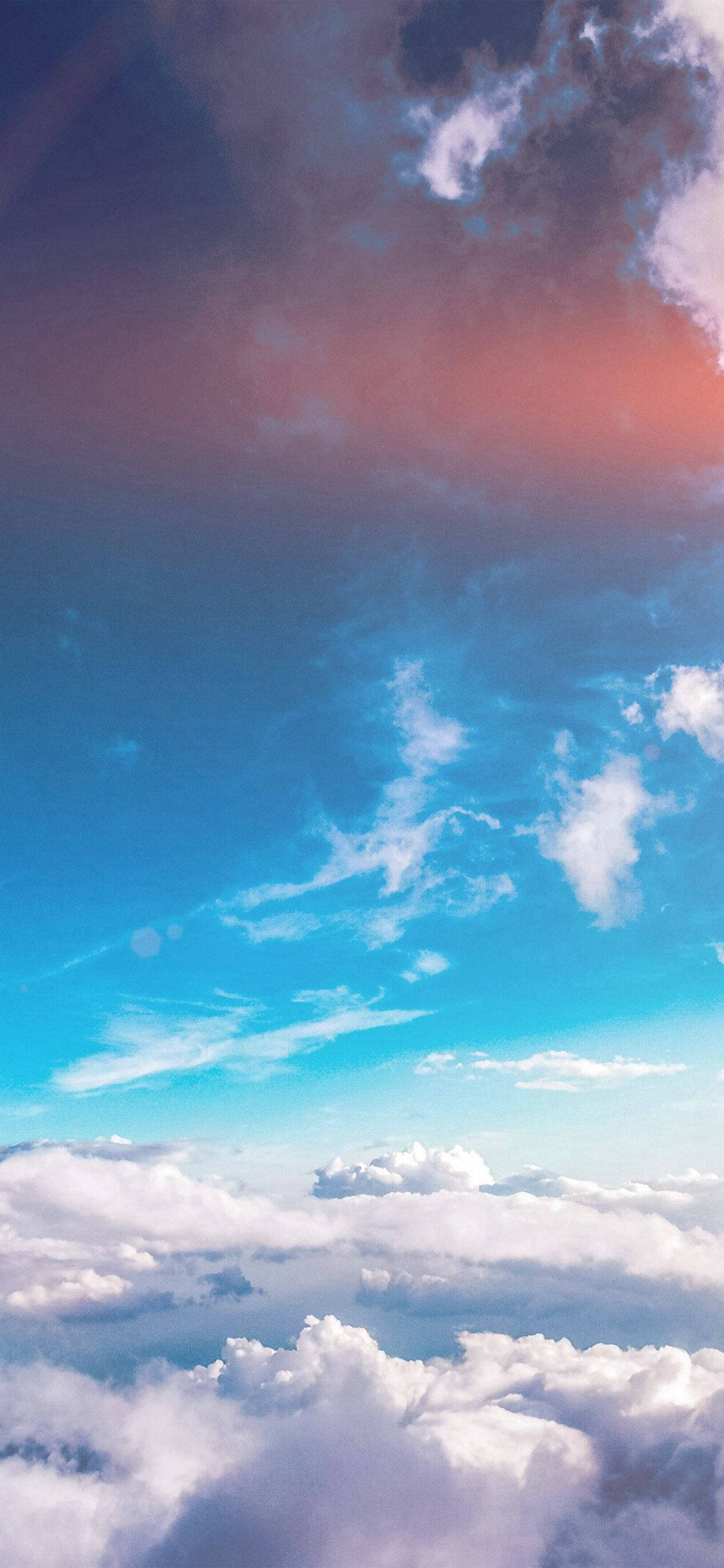 Blue Aesthetic Phone 桌布 壁紙 — 從高空俯瞰，蓬鬆的白雲下是充滿活力的藍天，天空染上粉紅和紫色的日落色彩。