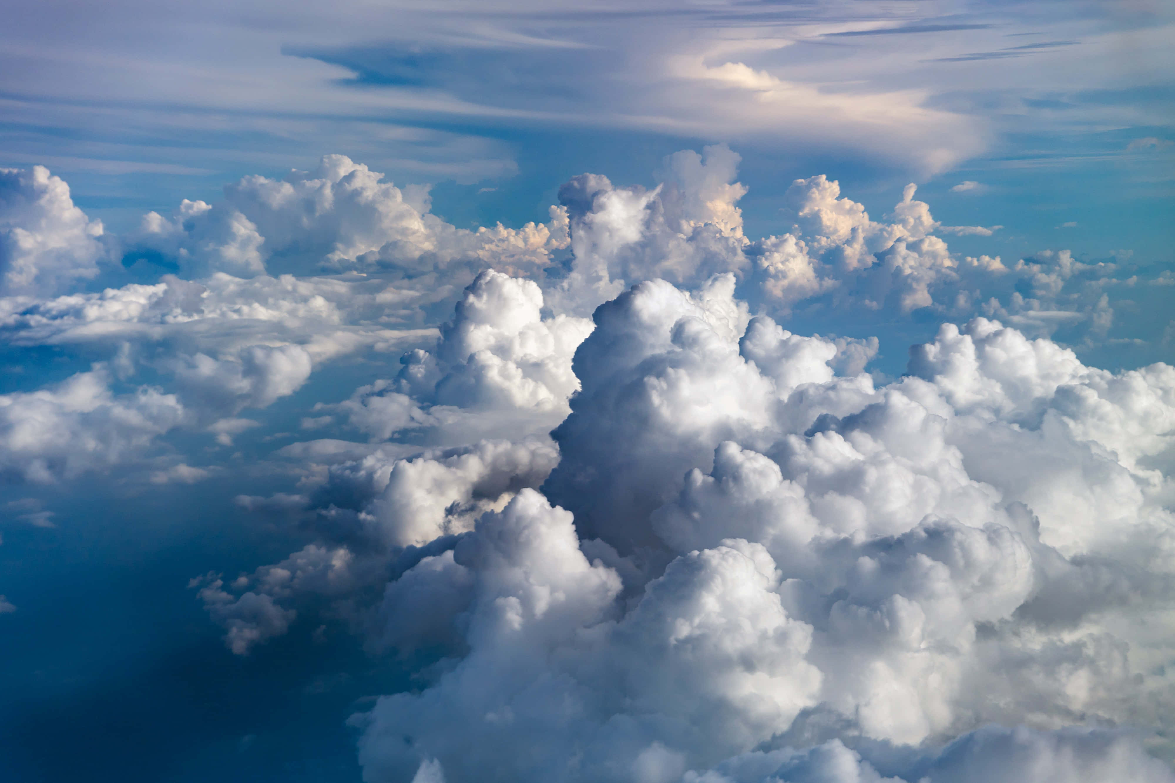 Clouds Aesthetics 桌布 壁紙 — 從高空俯瞰，蓬鬆的白雲在充滿活力的藍天中飄移，柔和的金色陽光突顯出它們紋理分明的頂峰。