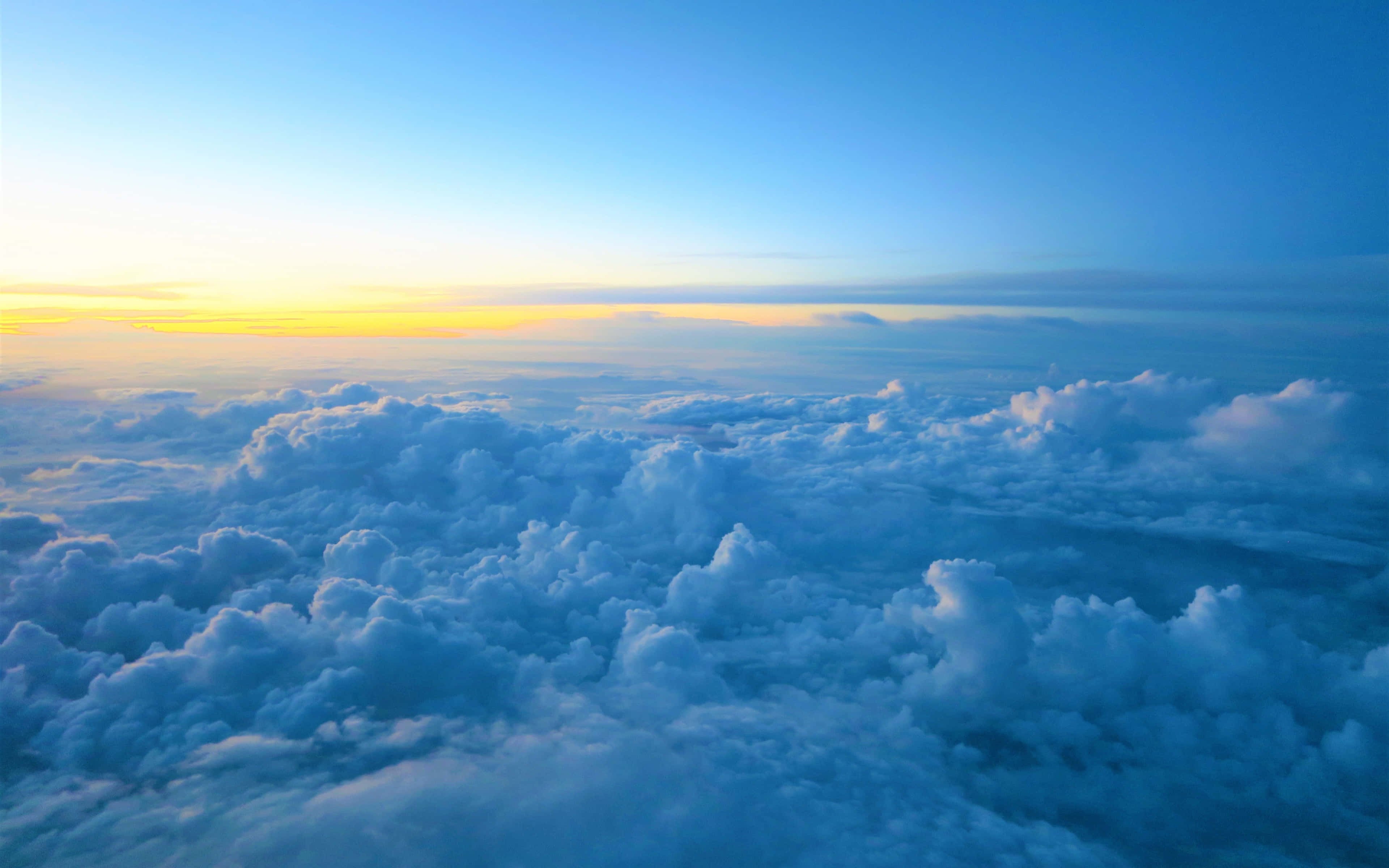 Clouds 4K 桌布 壁紙 — 從高空俯瞰，蓬鬆的白雲沐浴在金色日出光芒中，映襯著漸變的藍天。