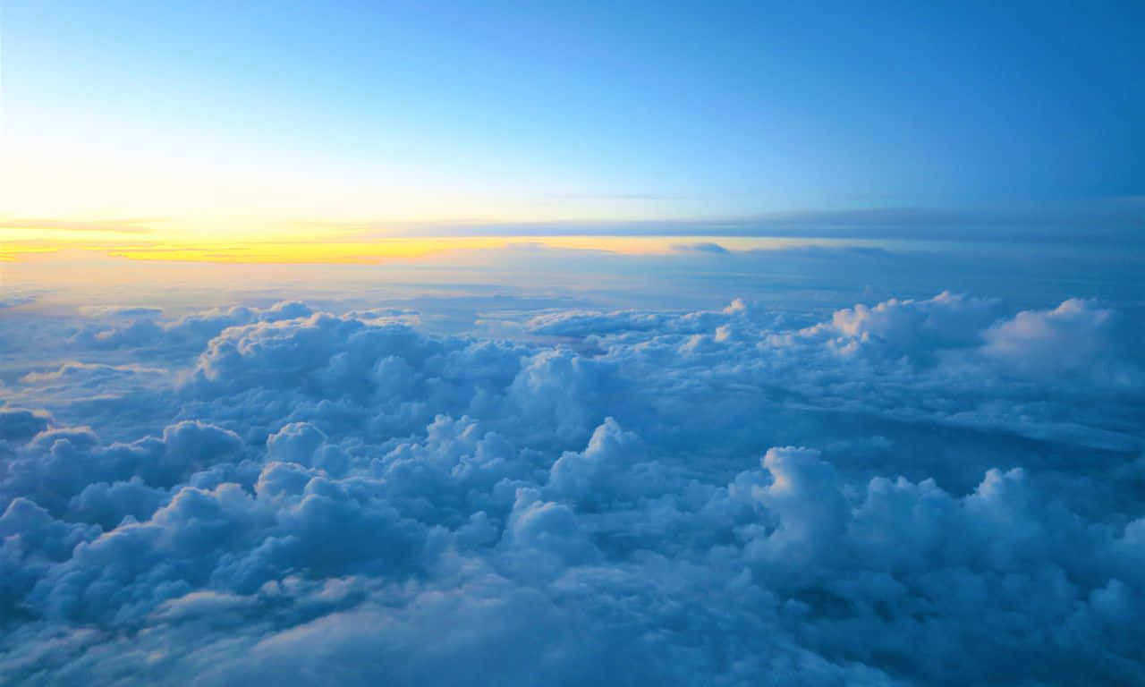1280x768 桌布 壁紙 — 從高空俯瞰，蓬鬆的白雲沐浴在金黃色的日出光芒中，背景是漸變的藍天。