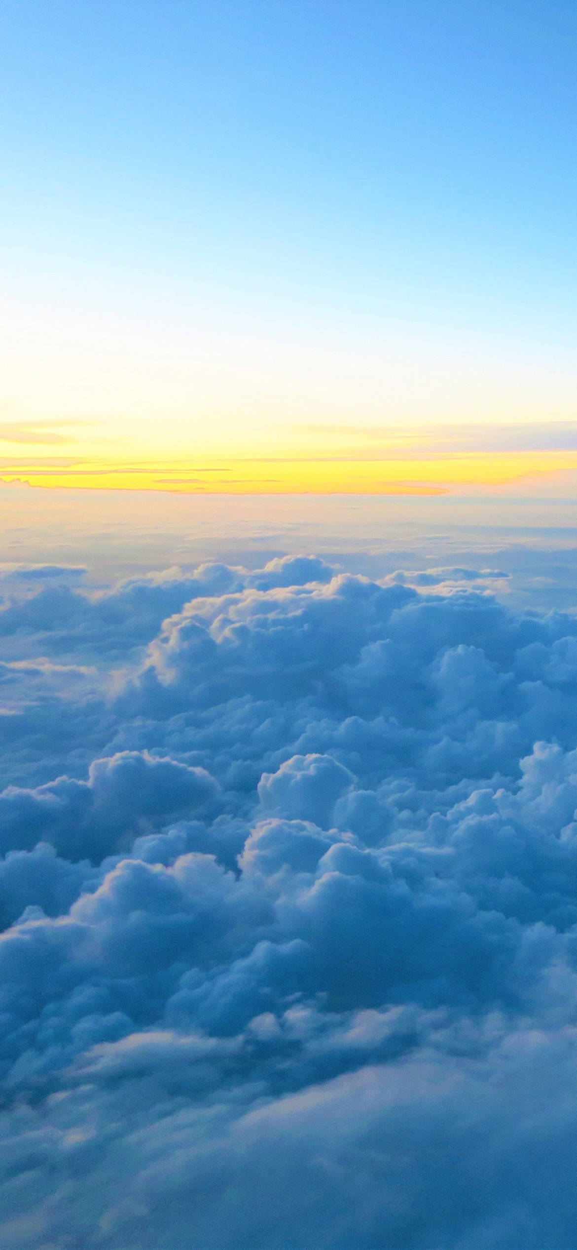Clouds Phone 桌布 壁紙 — 從高空俯瞰，蓬鬆的藍色雲朵沐浴在金色日出光芒中，映襯著清澈的天空。