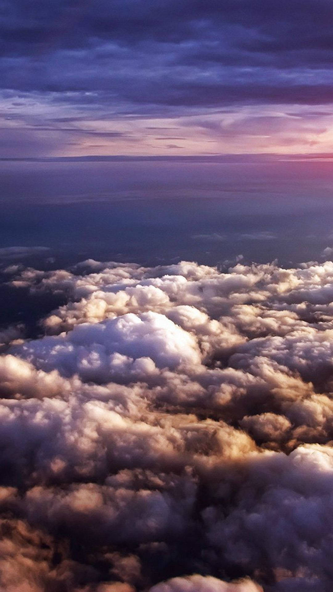 View 桌布 壁紙 — 從高空俯瞰，蓬鬆的雲朵沐浴在金黃色的日落光芒中，映襯著深紫色的暮色天空。
