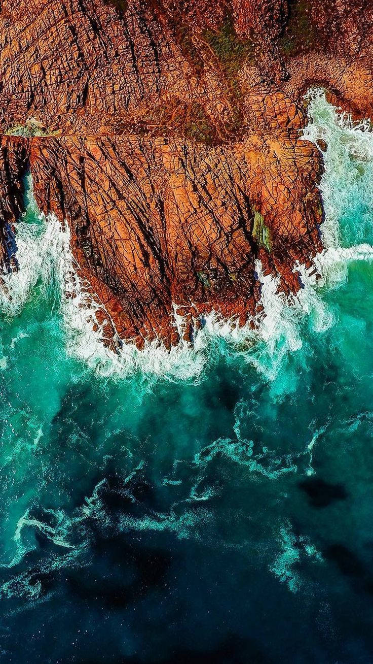 iPhone 桌布 壁紙 — 從高空俯瞰，藍綠色海浪拍打崎嶇的橙色懸崖，激起白色泡沫。