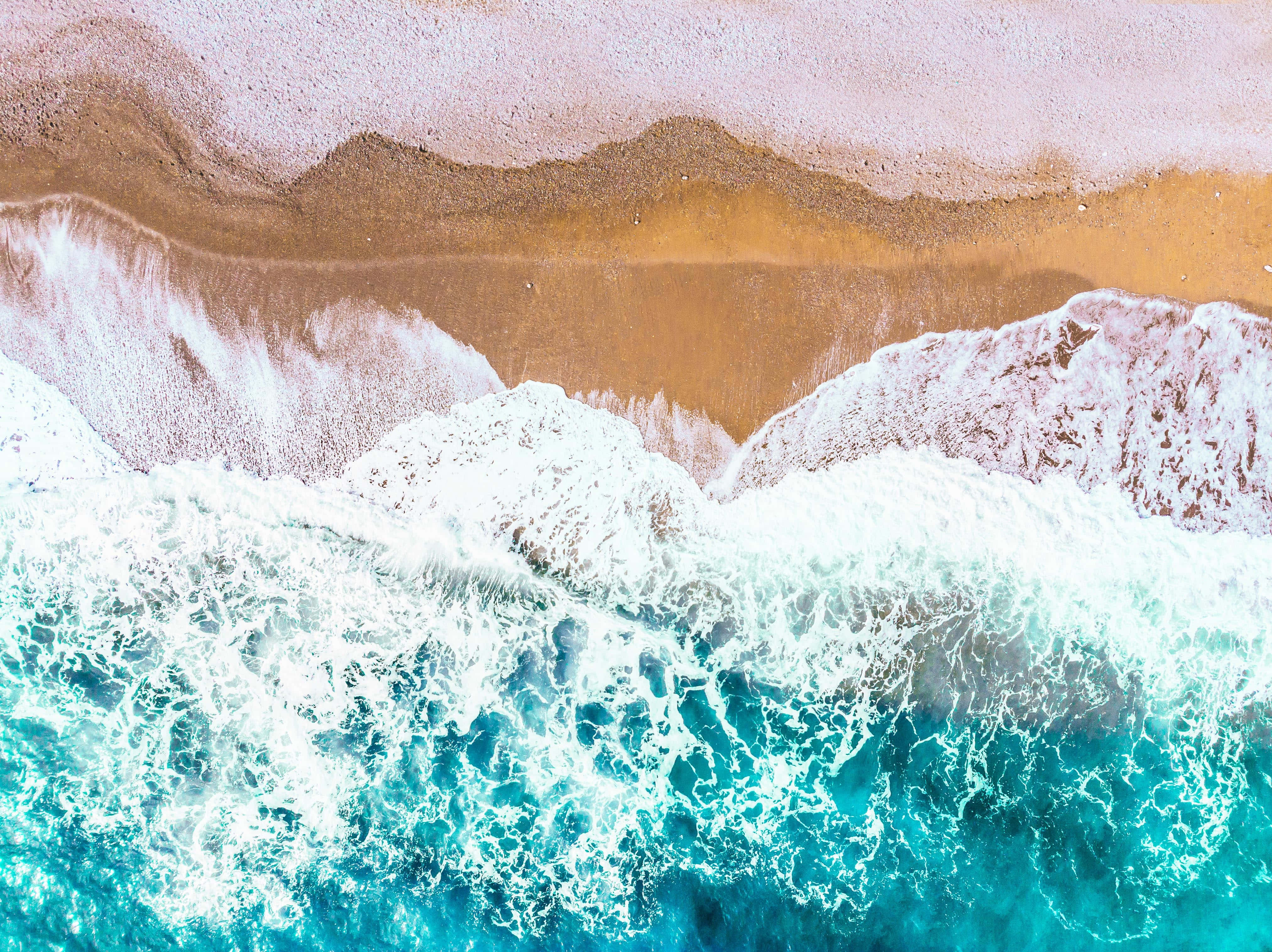 Twitter Header 桌布 壁紙 — 從高空俯瞰，藍綠色海浪拍打沙灘，泛起白色泡沫，呈現層層泥土色調。