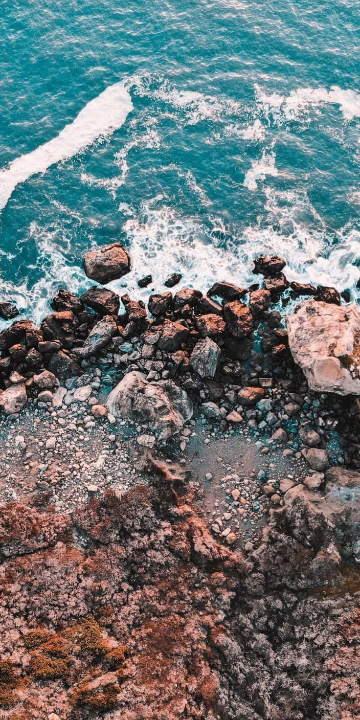 海灘 桌布 壁紙 — 從高空俯瞰，藍綠色海浪拍打著懸崖海岸線上崎嶇的紅褐色火山岩。