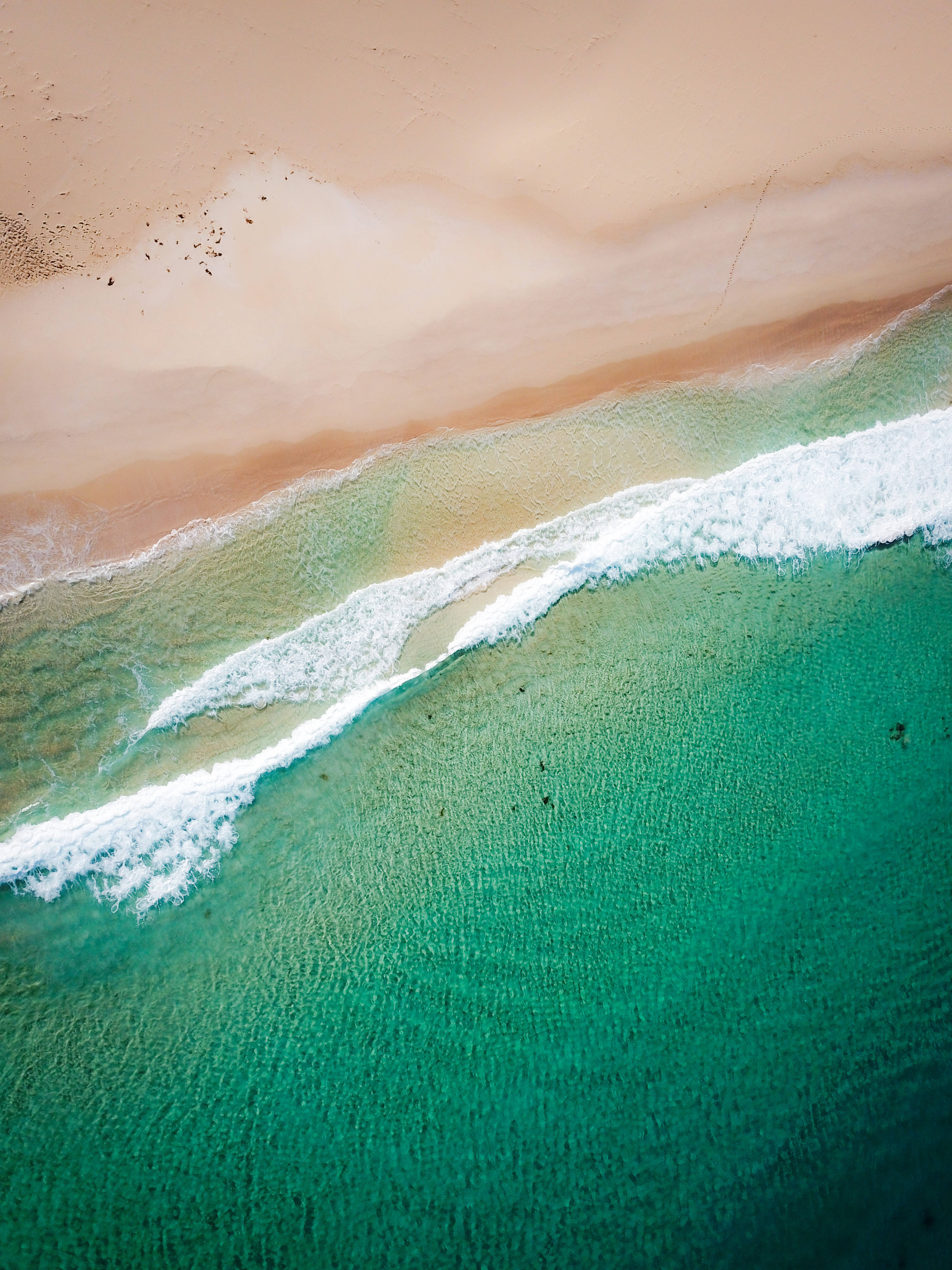 australia iPhone 桌布 壁紙 — 從高空俯瞰，青綠色的海浪拍打著柔軟的蜜桃色沙灘，呈現出清晰的水紋圖案。