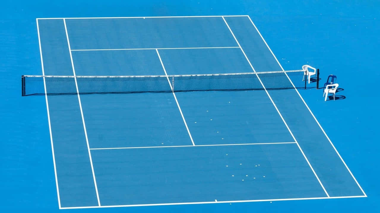 720p Tennis 桌布 壁紙 — 從高空俯瞰一個充滿活力的藍色硬地網球場，白色線條清晰，球場上散落著網球，在明亮的日光下。